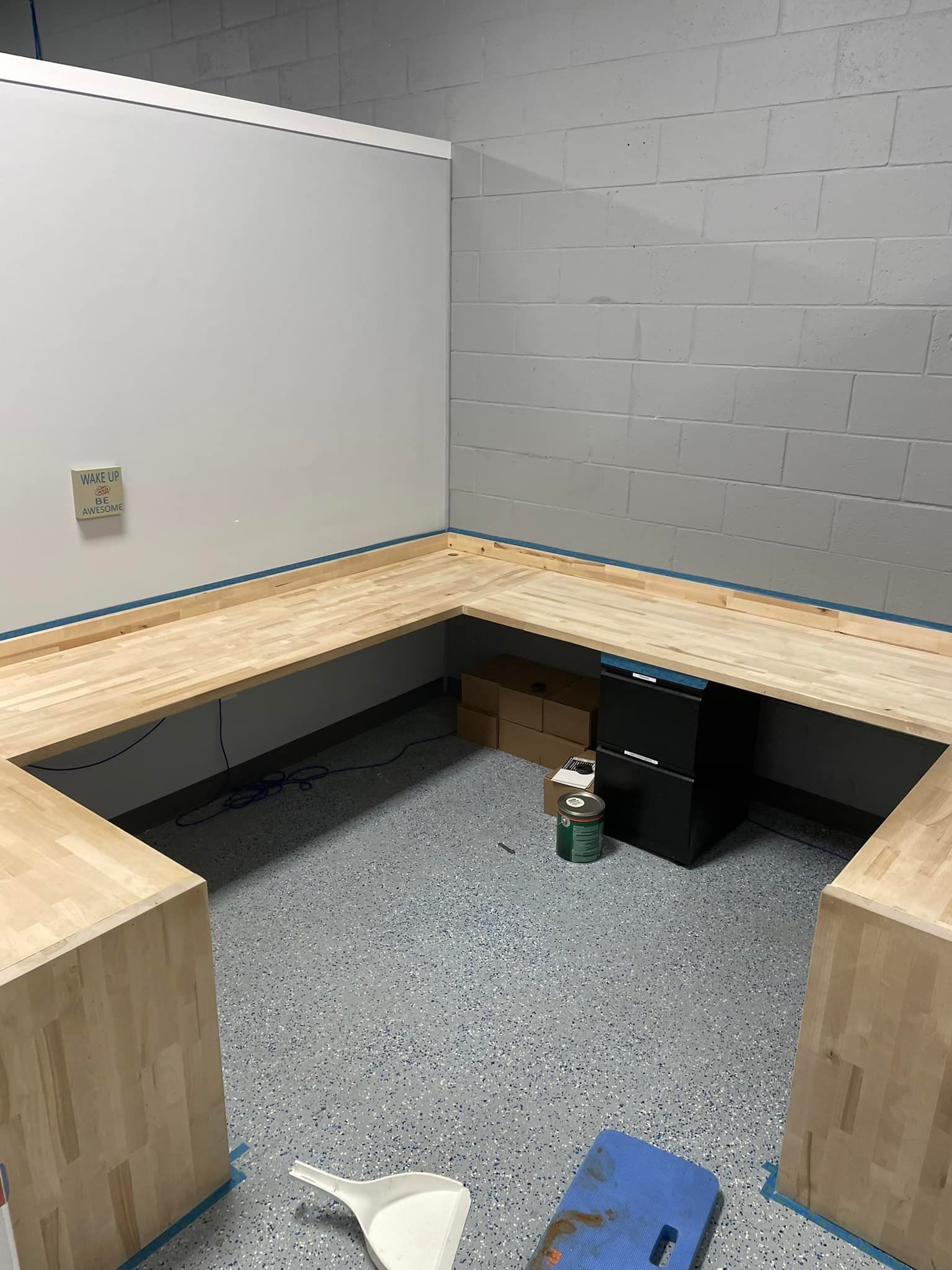 L-shaped wooden structure built in a room with a white wall, gray brick wall, and speckled gray floor.