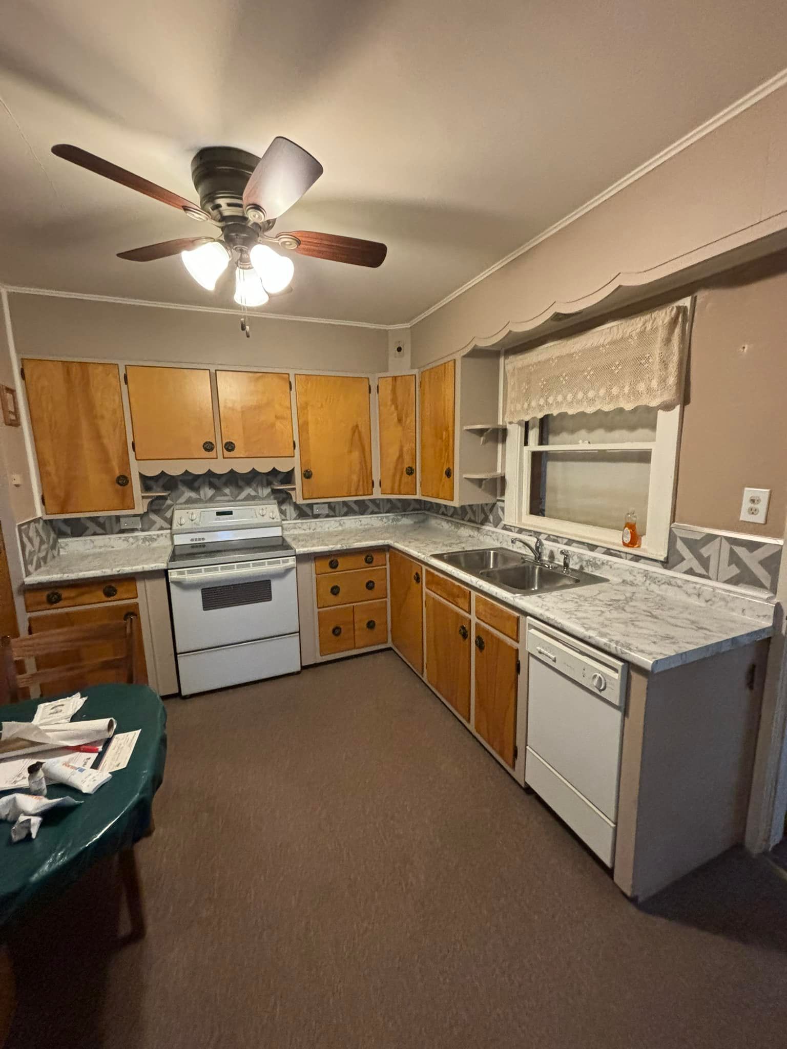 Kitchen with light wood cabinets, white appliances, and gray countertops. A green table is in the foreground.