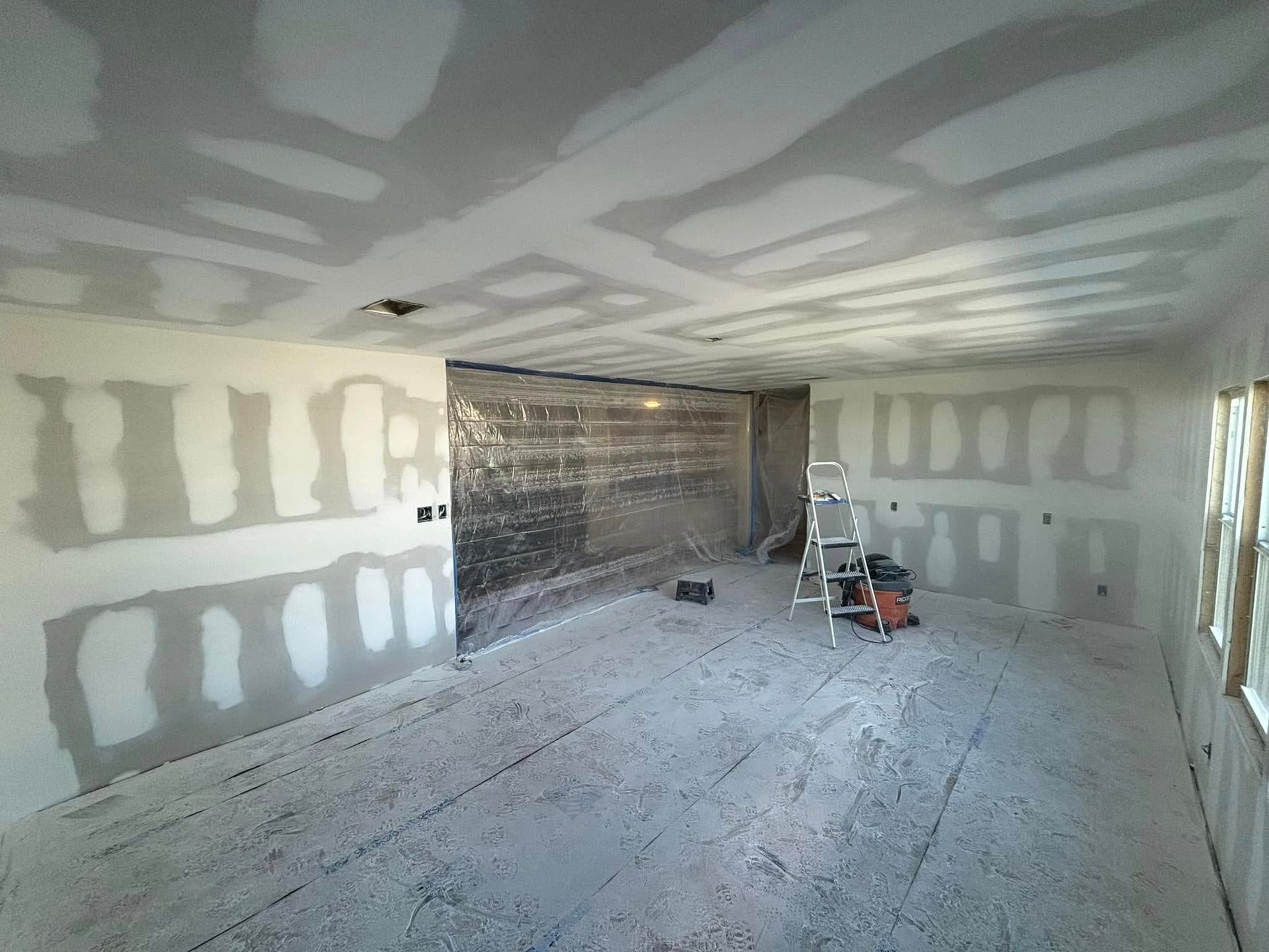 Interior room with drywall, taped seams, and construction materials on the floor.
