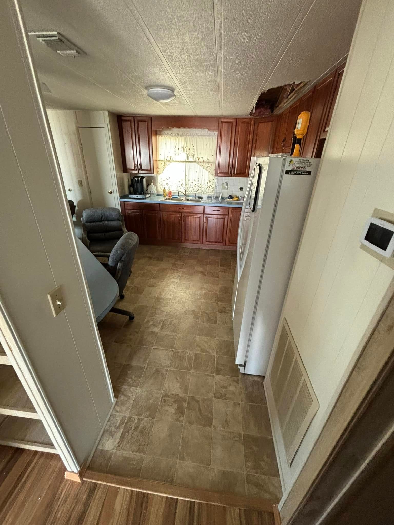 Kitchen with dark cabinets, white appliances, and a hallway to the left, visible flooring.
