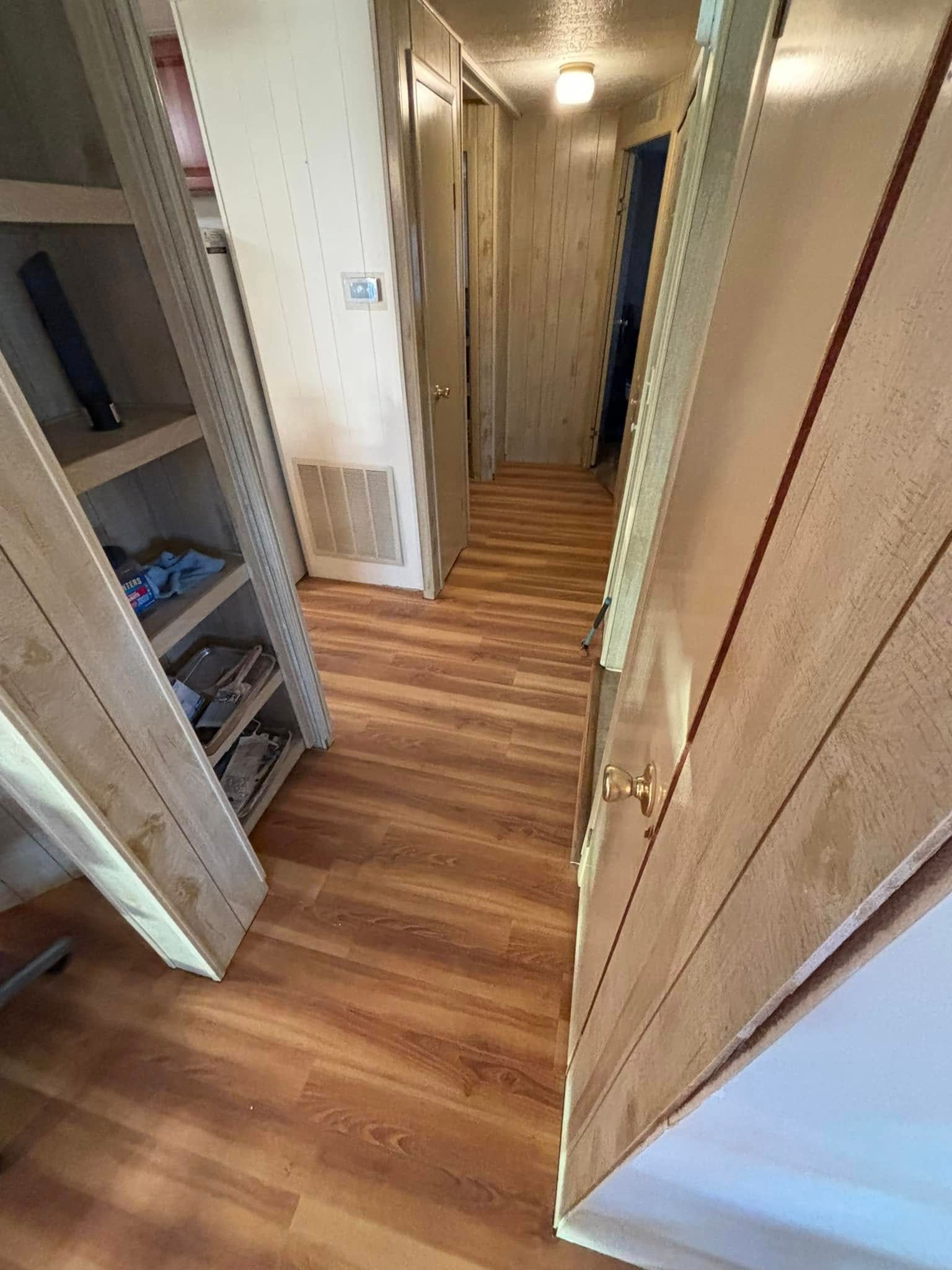 Narrow hallway with wood-look flooring, built-in shelves on left, doors on right and down the hall.