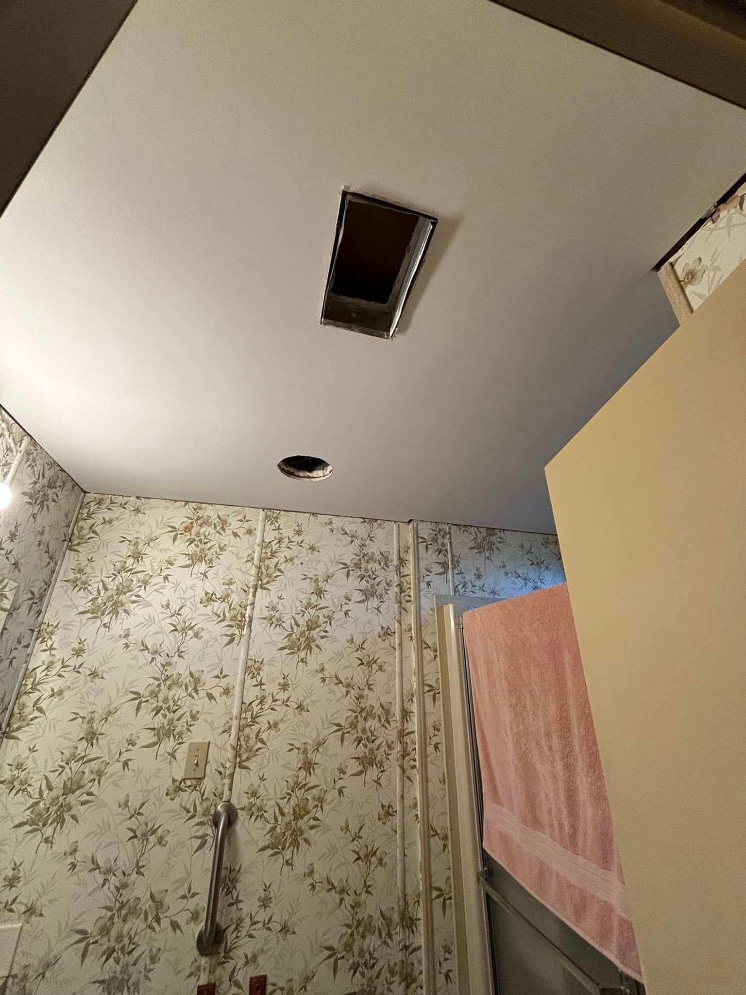 Bathroom ceiling with rectangular opening and a circular fixture. Wallpapered wall.