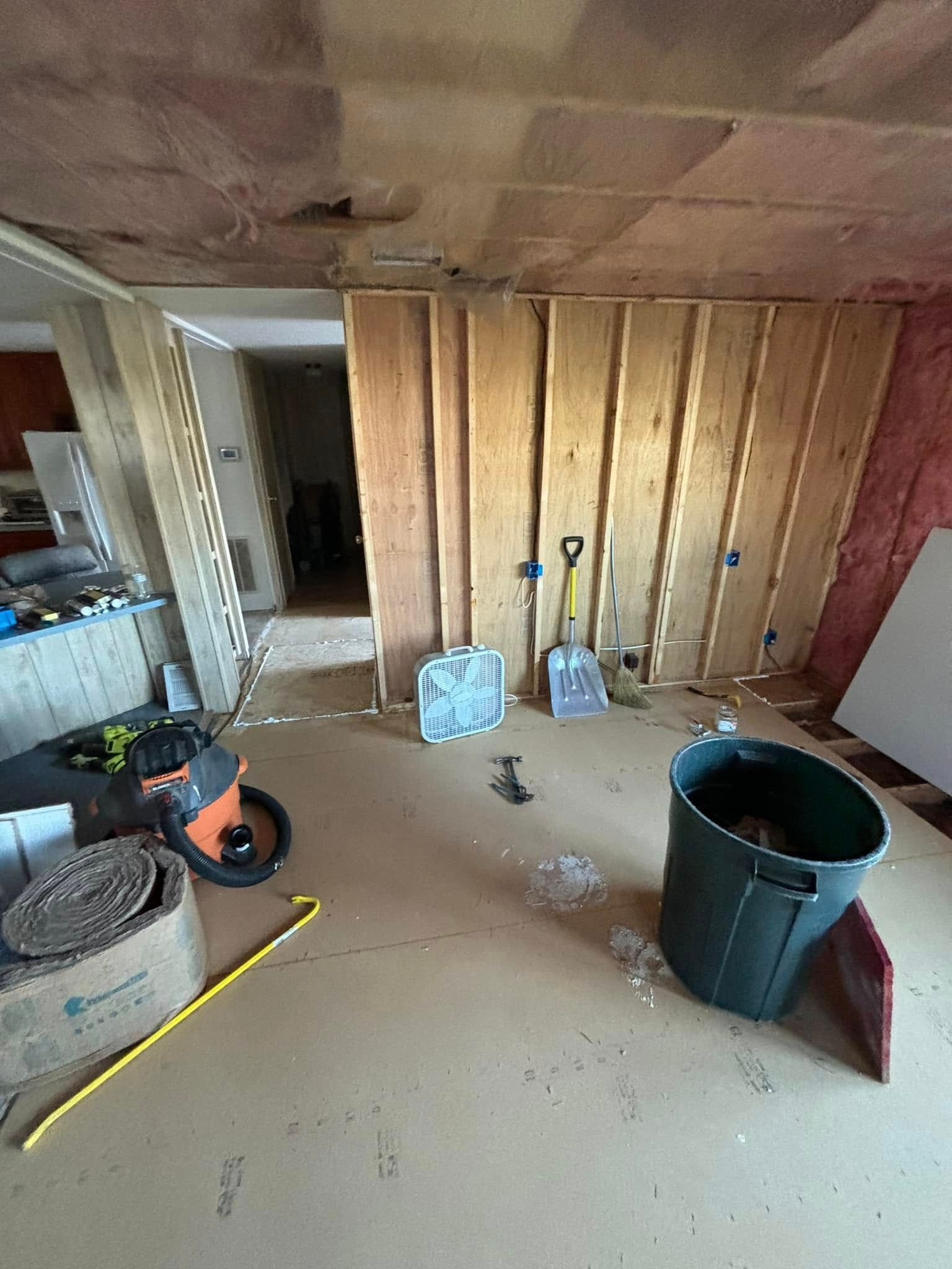 Interior of a room under construction with exposed wooden beams, studs, and construction debris.