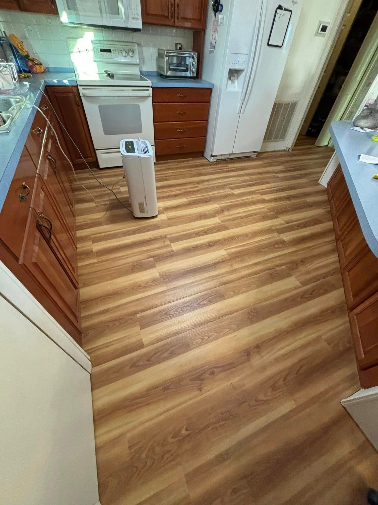 Kitchen with wood-look flooring. Cabinets and appliances are visible. An air purifier stands near the oven.