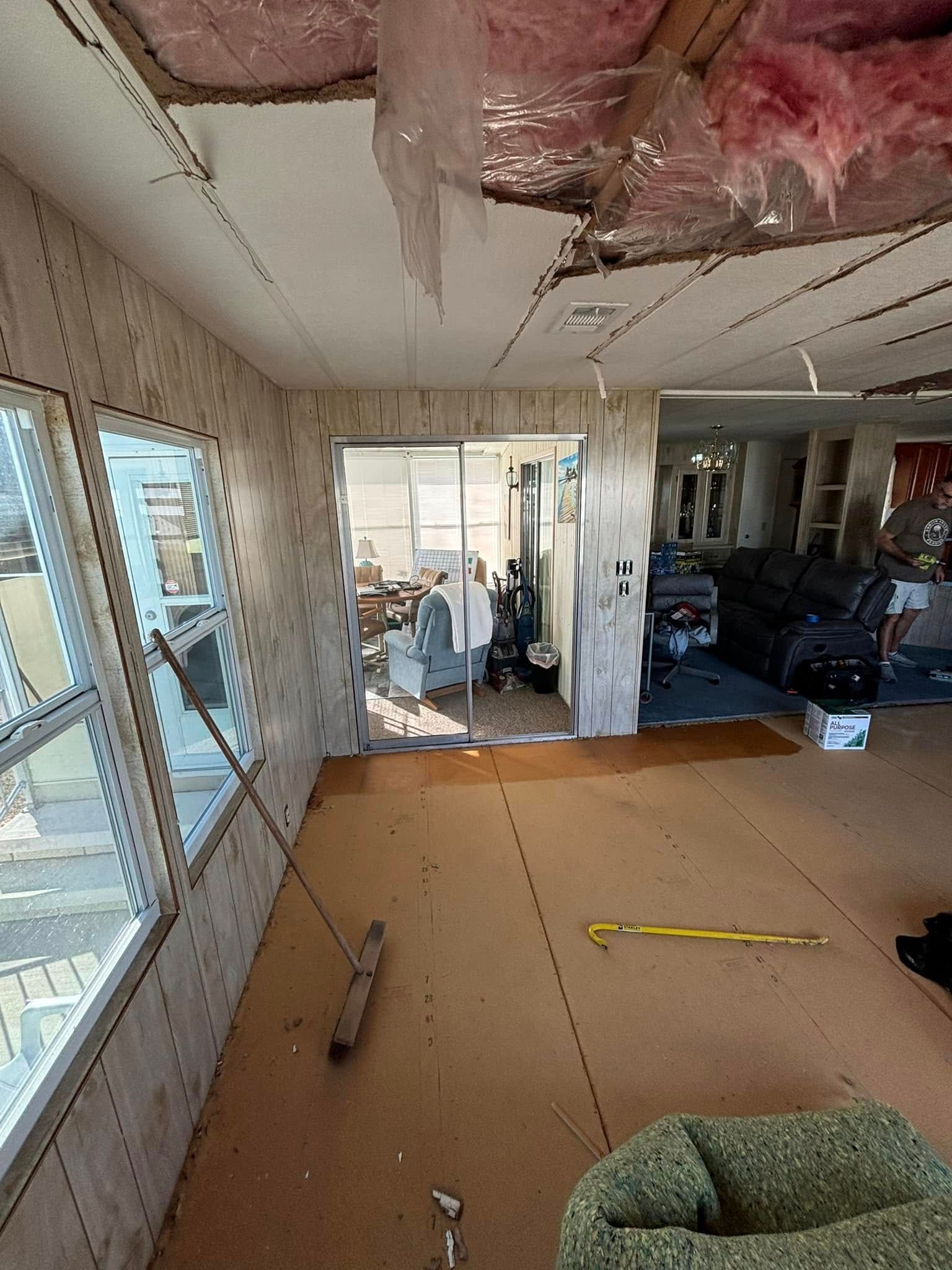 Interior view of a room under renovation with exposed ceiling insulation. A sliding glass door leads to an outside area.