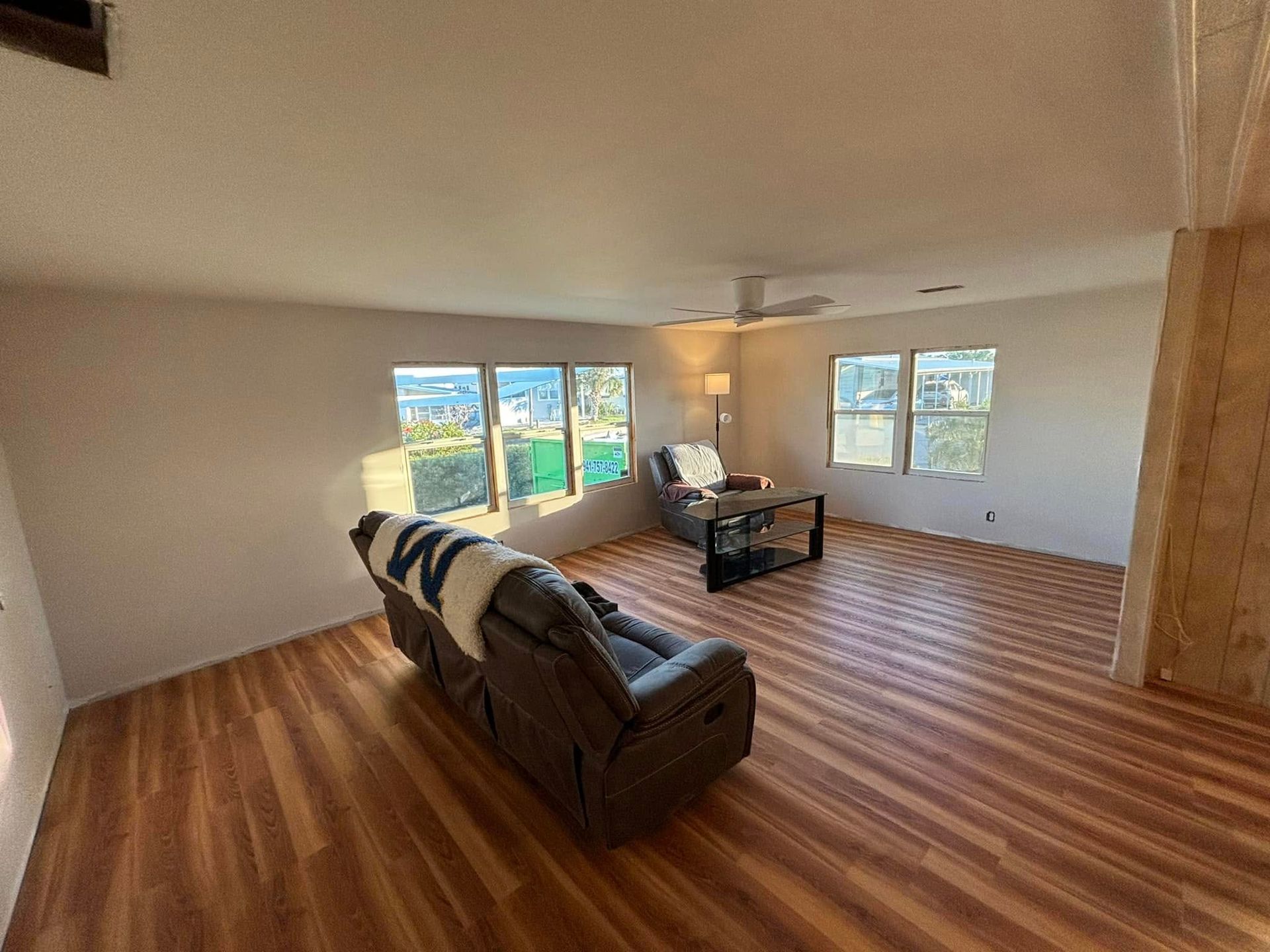 Living room with recliner, two chairs, windows, and wood-look flooring.