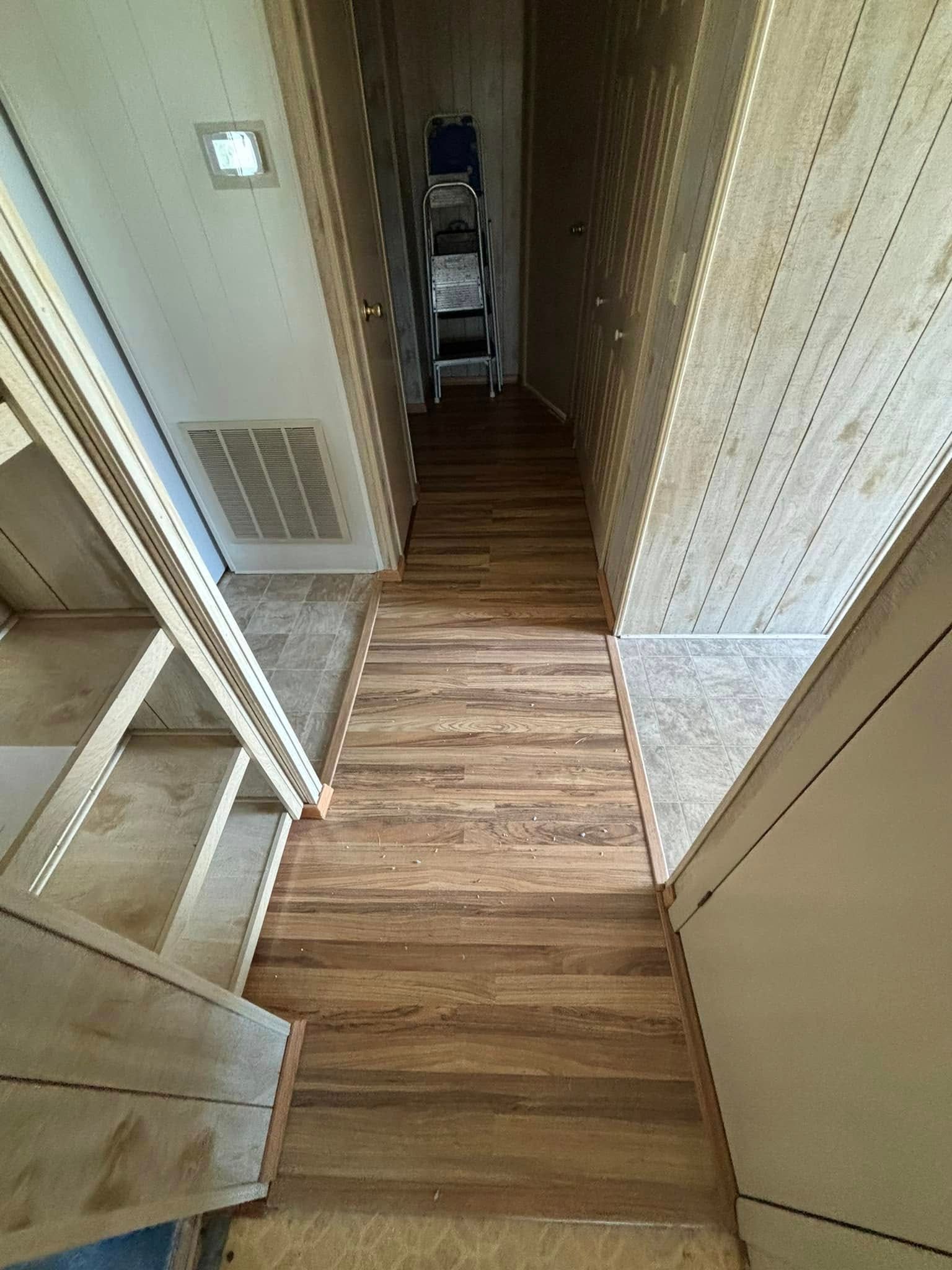 Narrow wooden staircase leading up, flanked by walls and shelves. A ladder sits at the top.