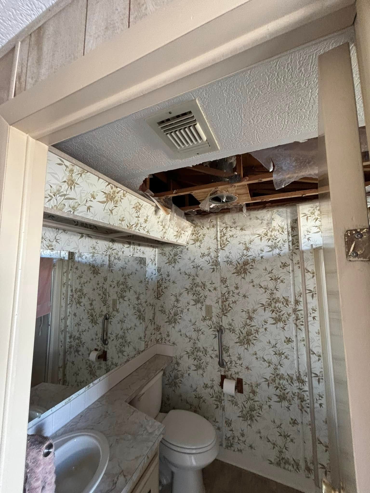 Bathroom interior with water damage to the ceiling and floral wallpaper, showing toilet and sink.