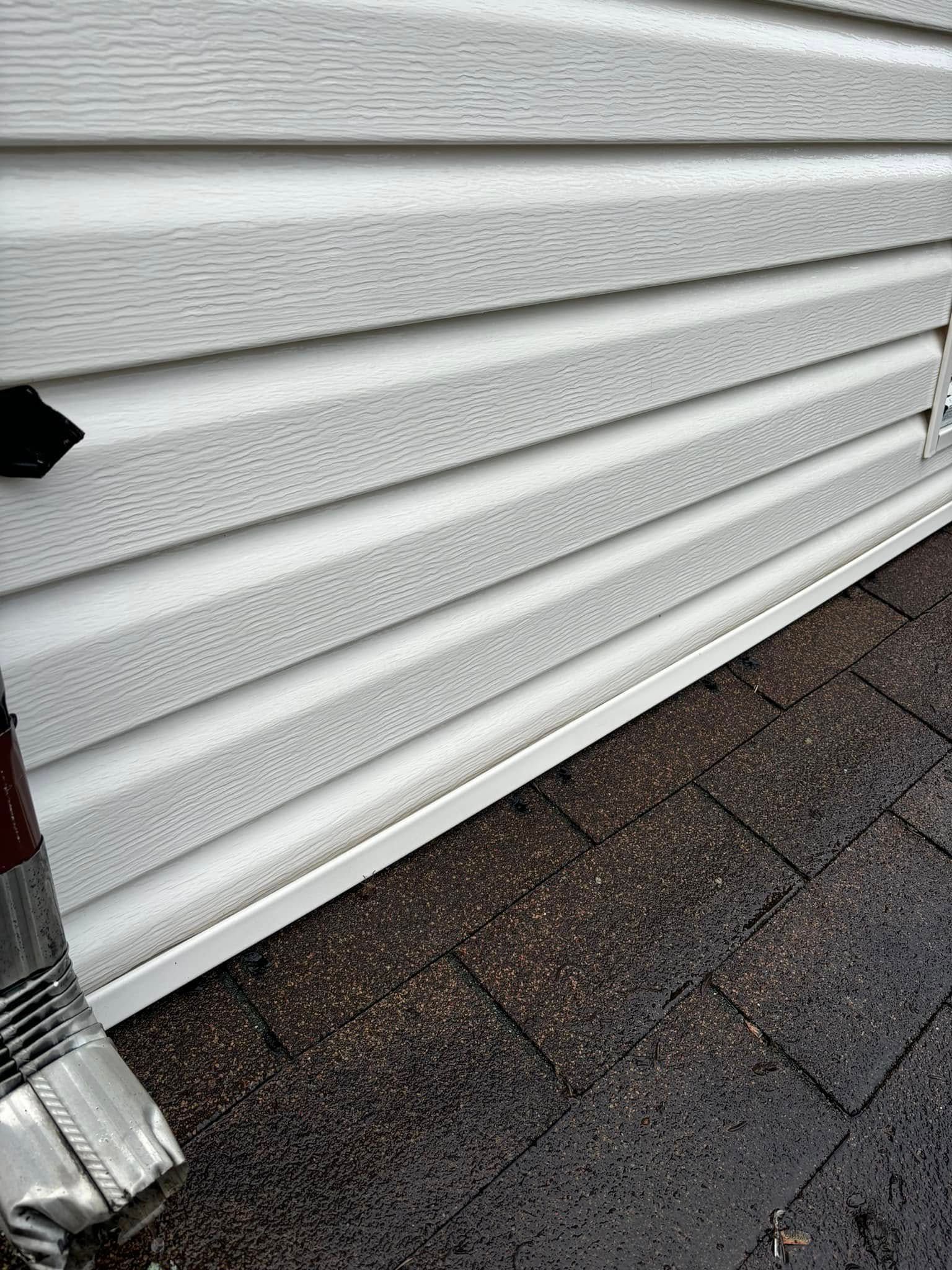 White vinyl siding on a building, with a gutter and roof visible.