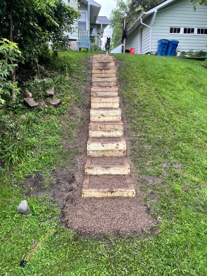 Wooden steps ascend a grassy hill. A dog stands at the top.