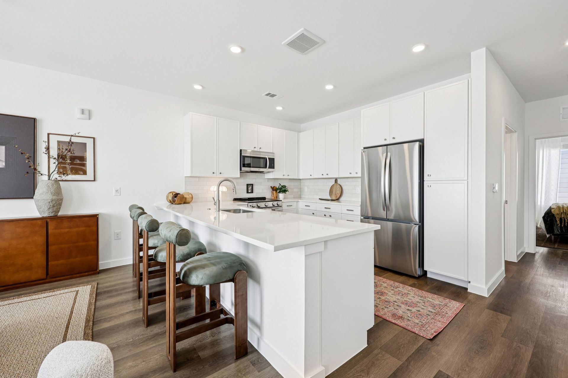 Modern kitchen with a white island, bar stools, stainless steel appliances, and wood flooring.