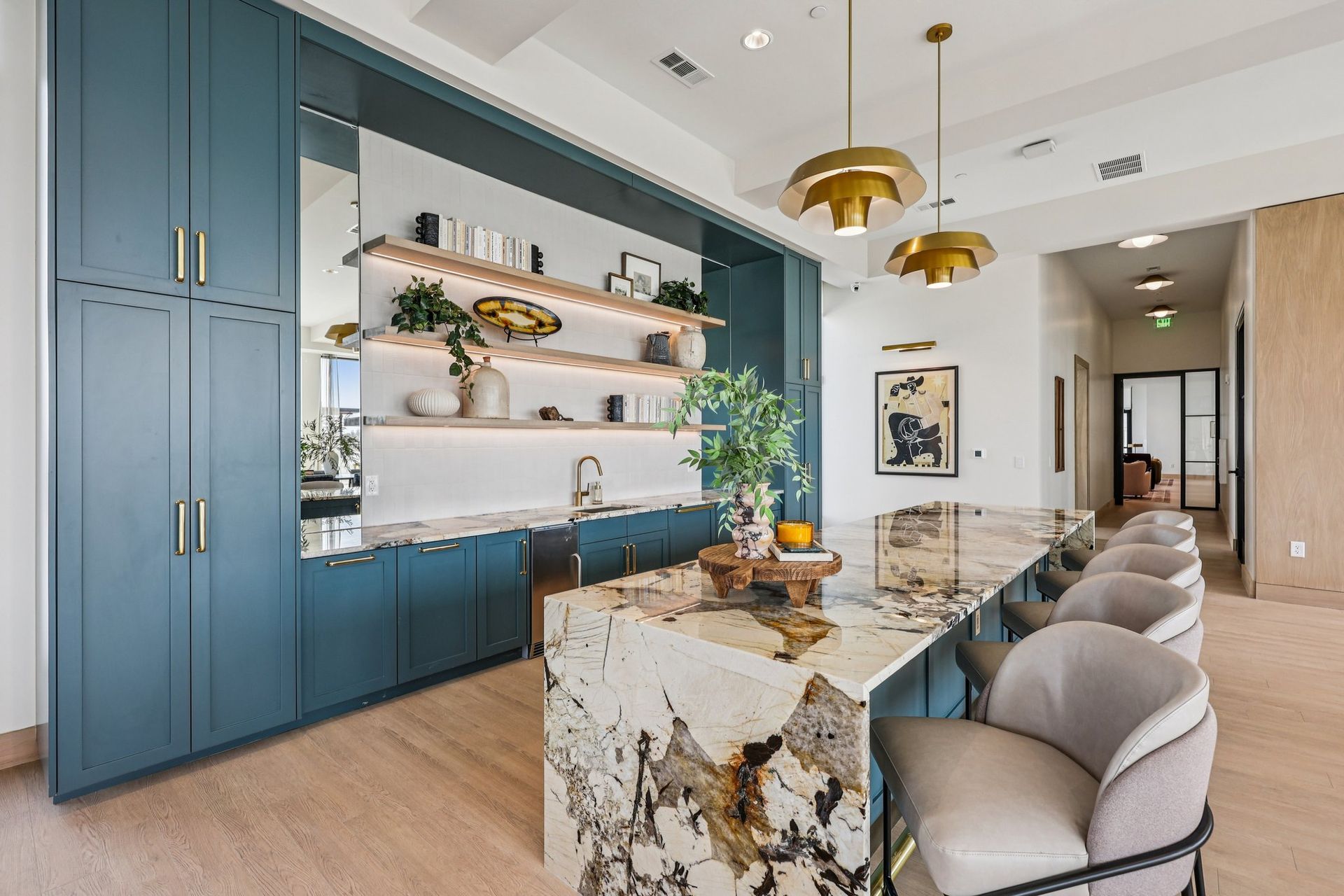 A modern kitchen area featuring blue cabinetry, a stone island with bar seating, and open shelving with plants.