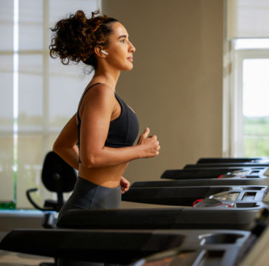 Woman runs on a treadmill in a gym, wearing a sports bra and leggings.
