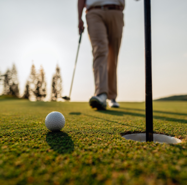 Golf ball near the hole, golfer walking on green. Sunny outdoor setting.