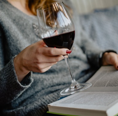 Woman holding a glass of red wine, reading a book.