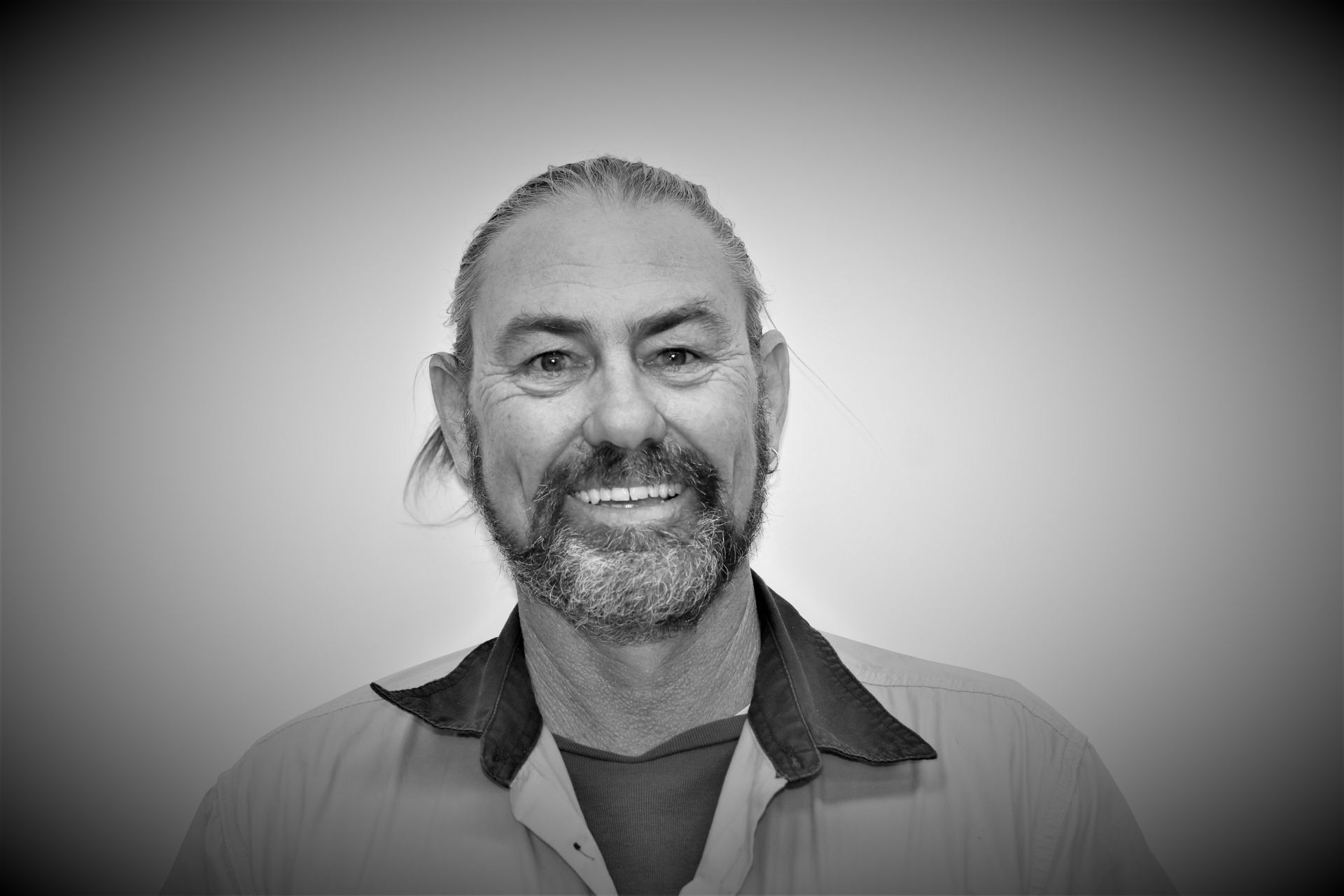 A man with a beard and long hair is smiling in a black and white photo.Image placeholder