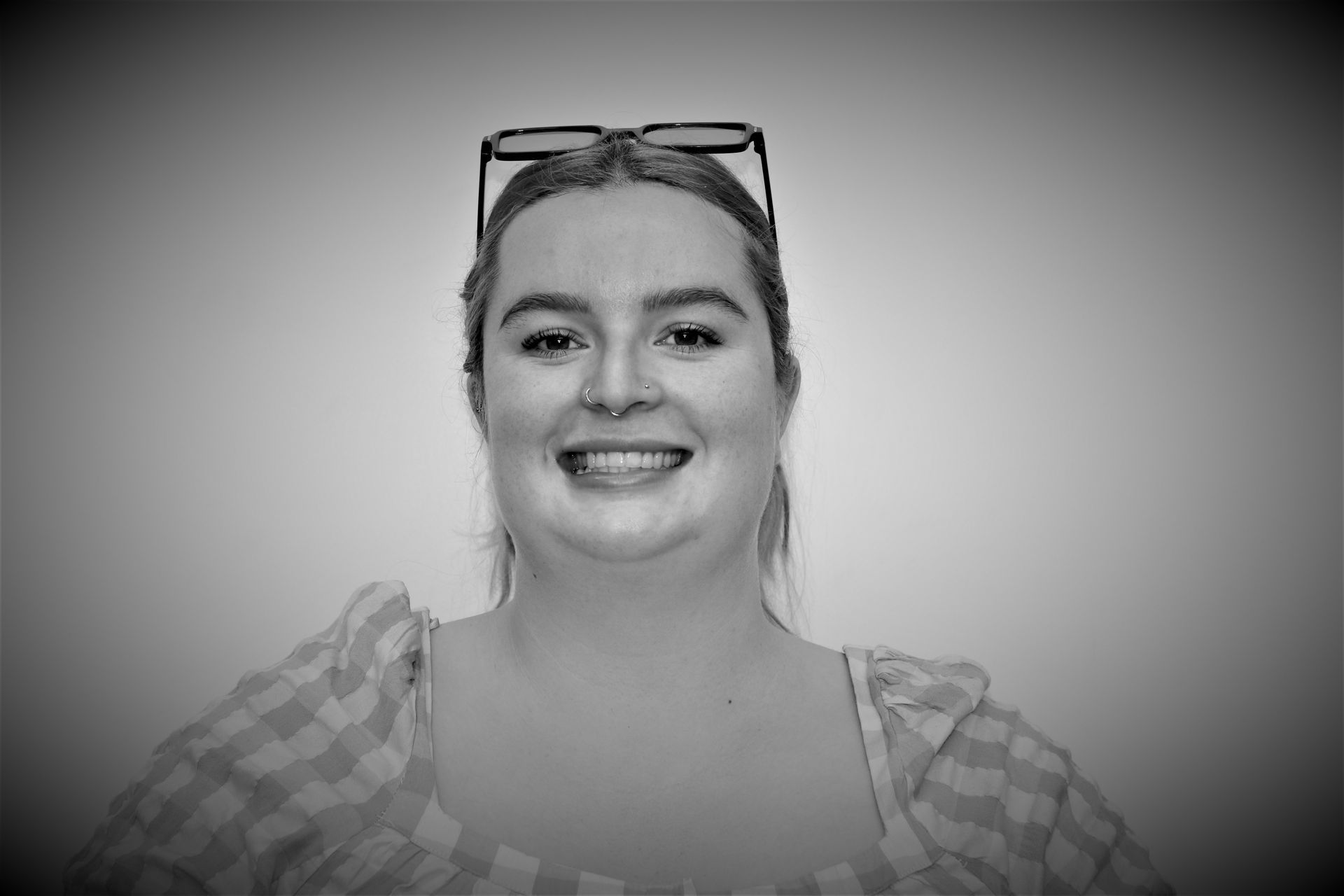 A woman wearing glasses is smiling in a black and white photo.