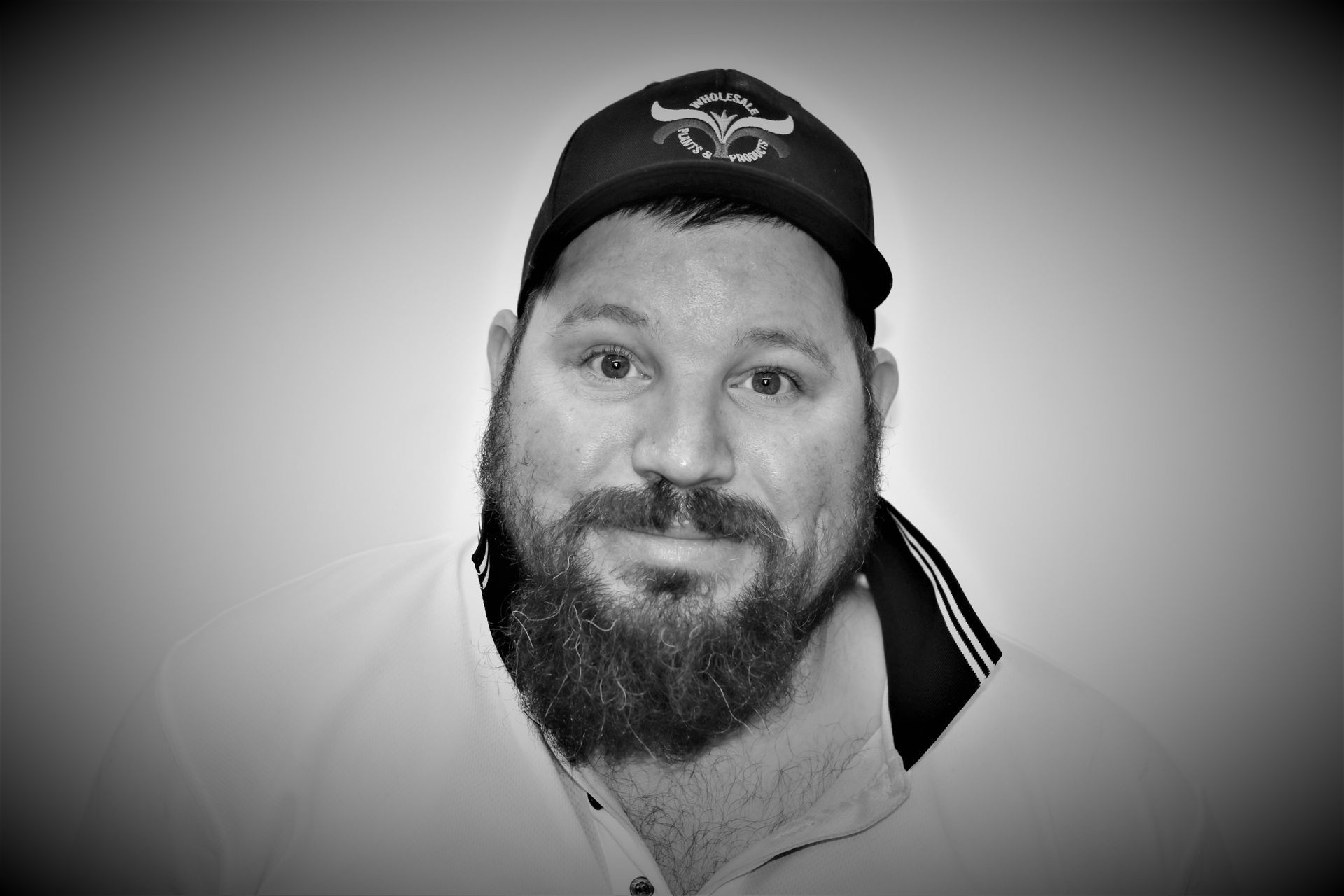 A man with a beard is wearing a hat and a white shirt.