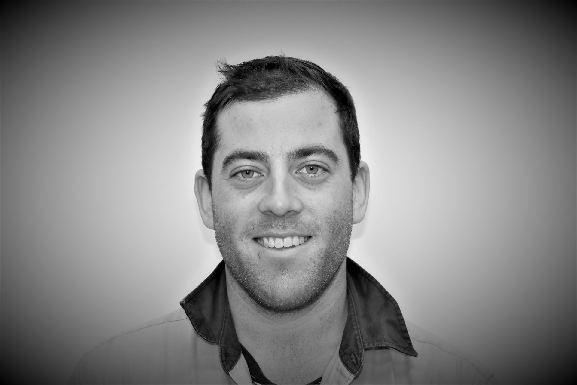 A man with a beard is smiling in a black and white photo.