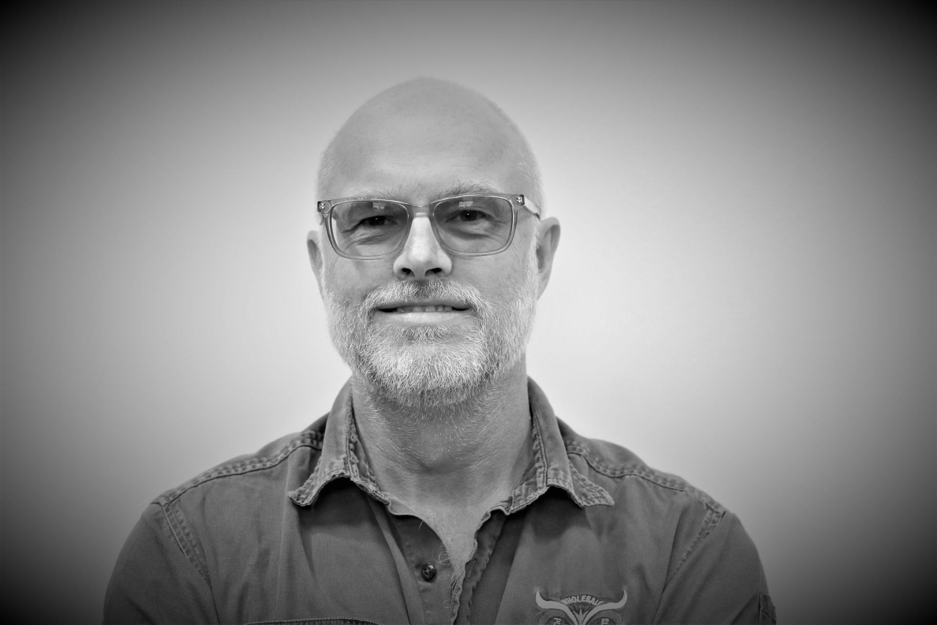 A black and white photo of a bald man with a beard and glasses.
