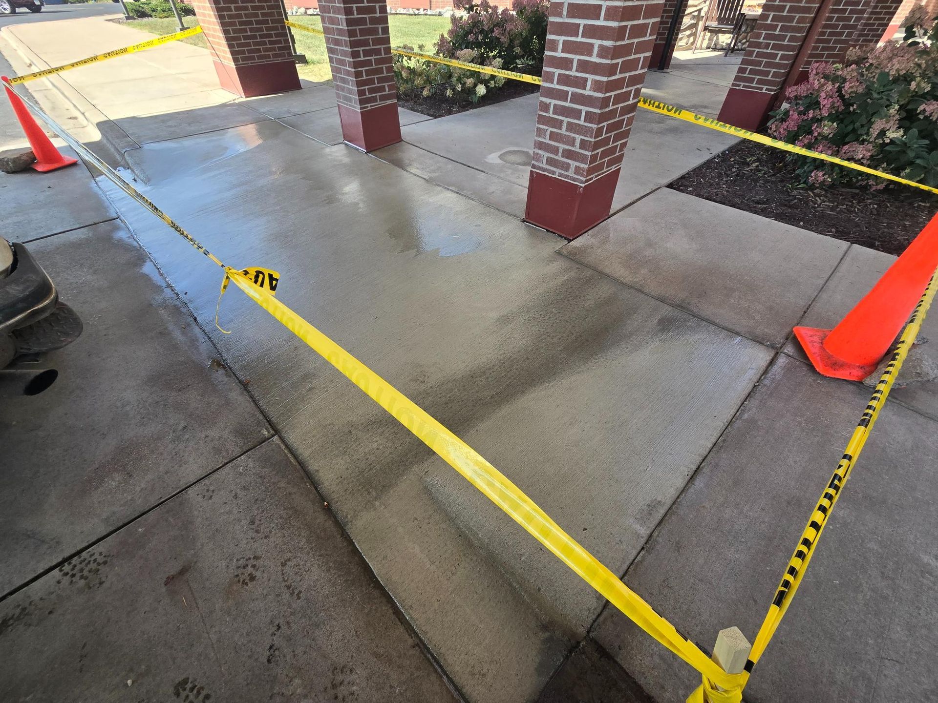 A concrete walkway with yellow tape and orange cones around it
