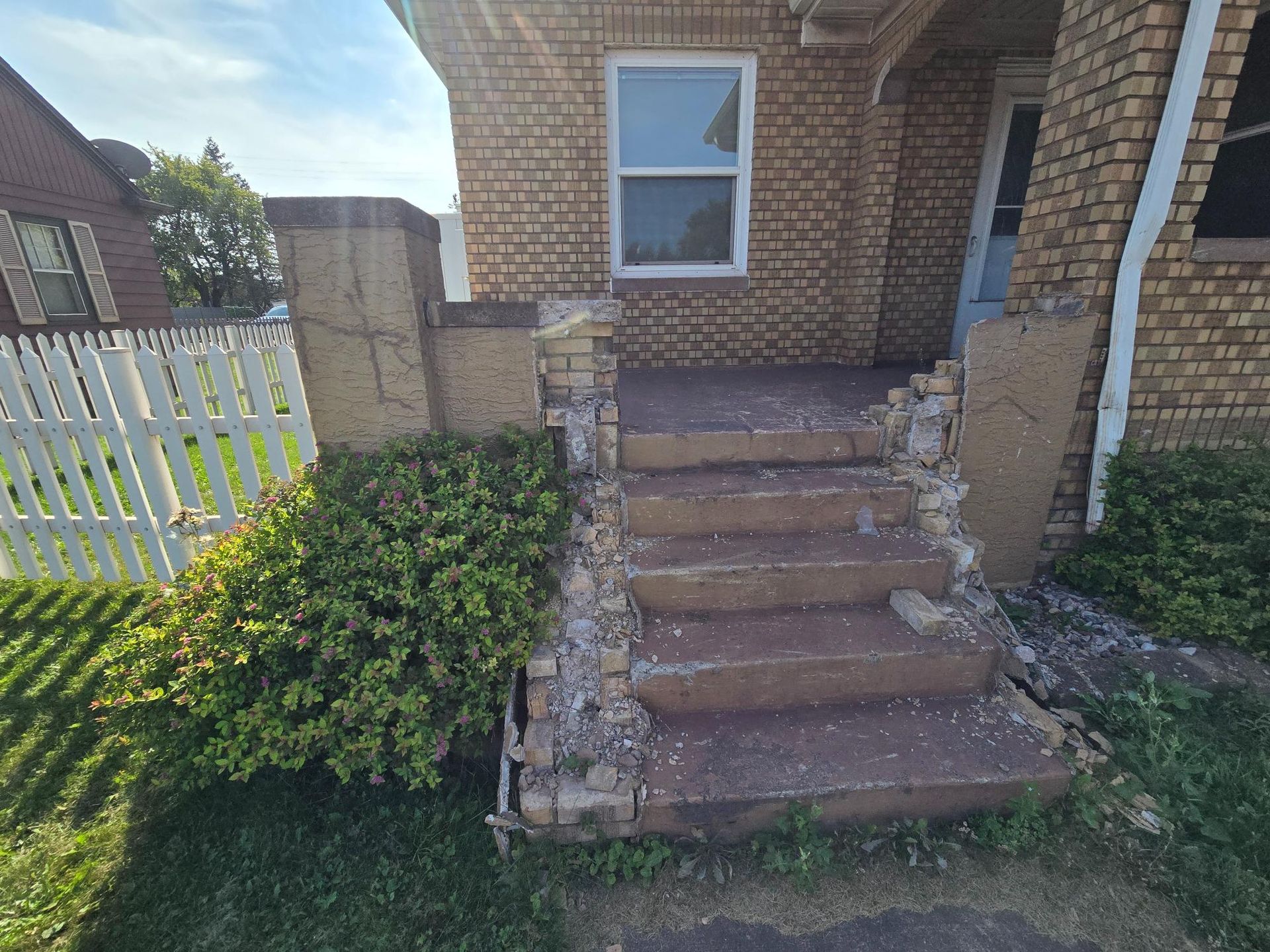 A brick house with a broken front porch and stairs.
