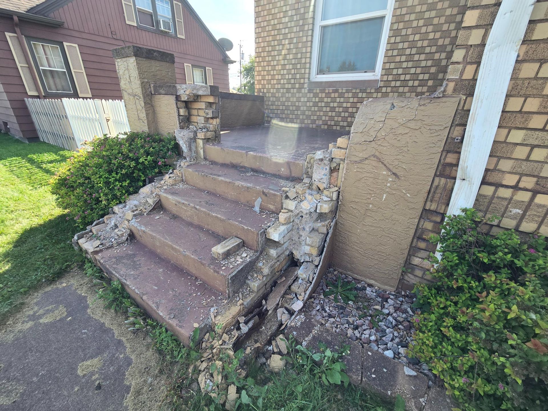 A brick house with a broken porch and stairs.