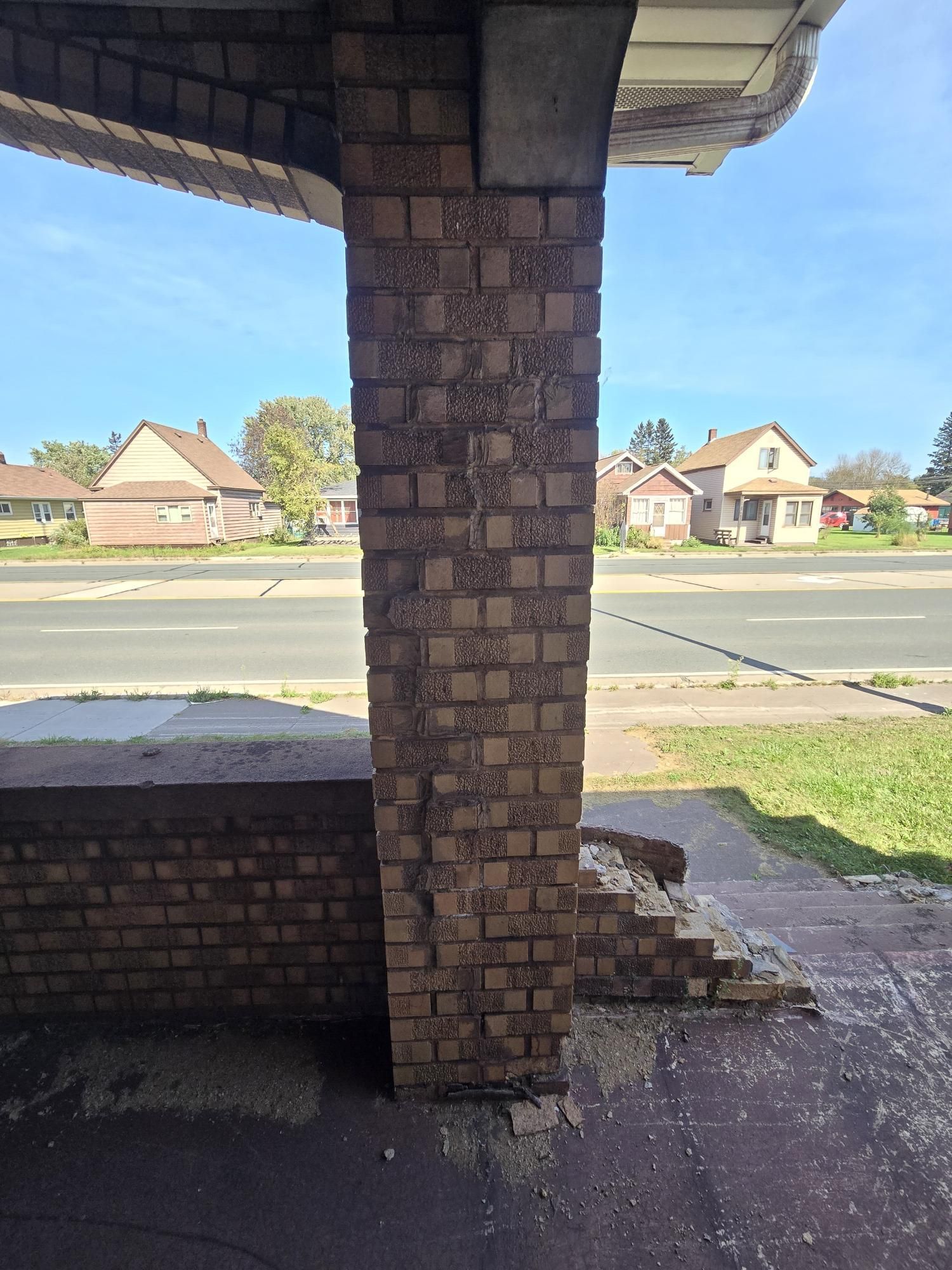 A brick column with a view of a street and houses in the background