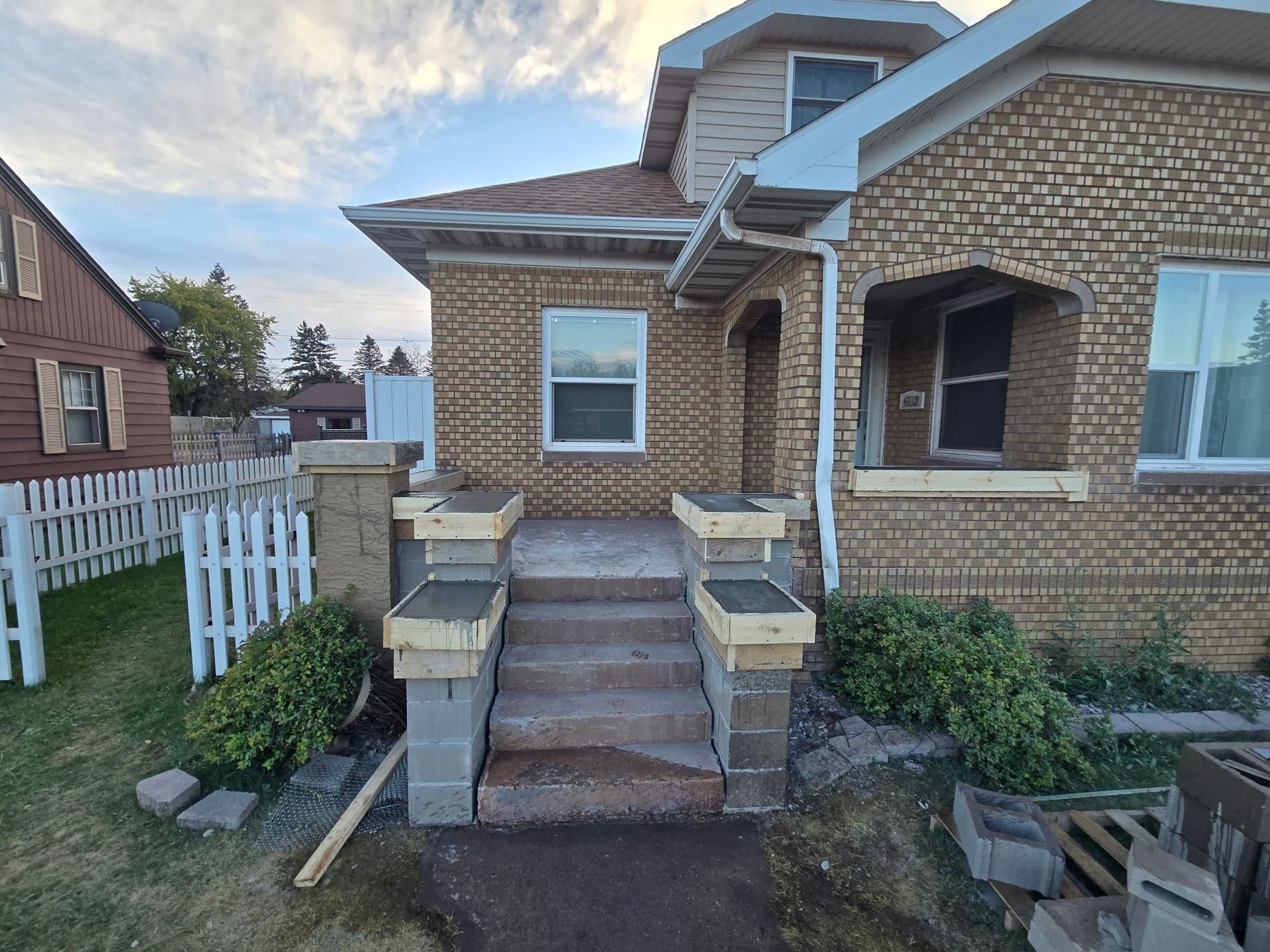 A brick house with stairs and a white picket fence in front of it.
