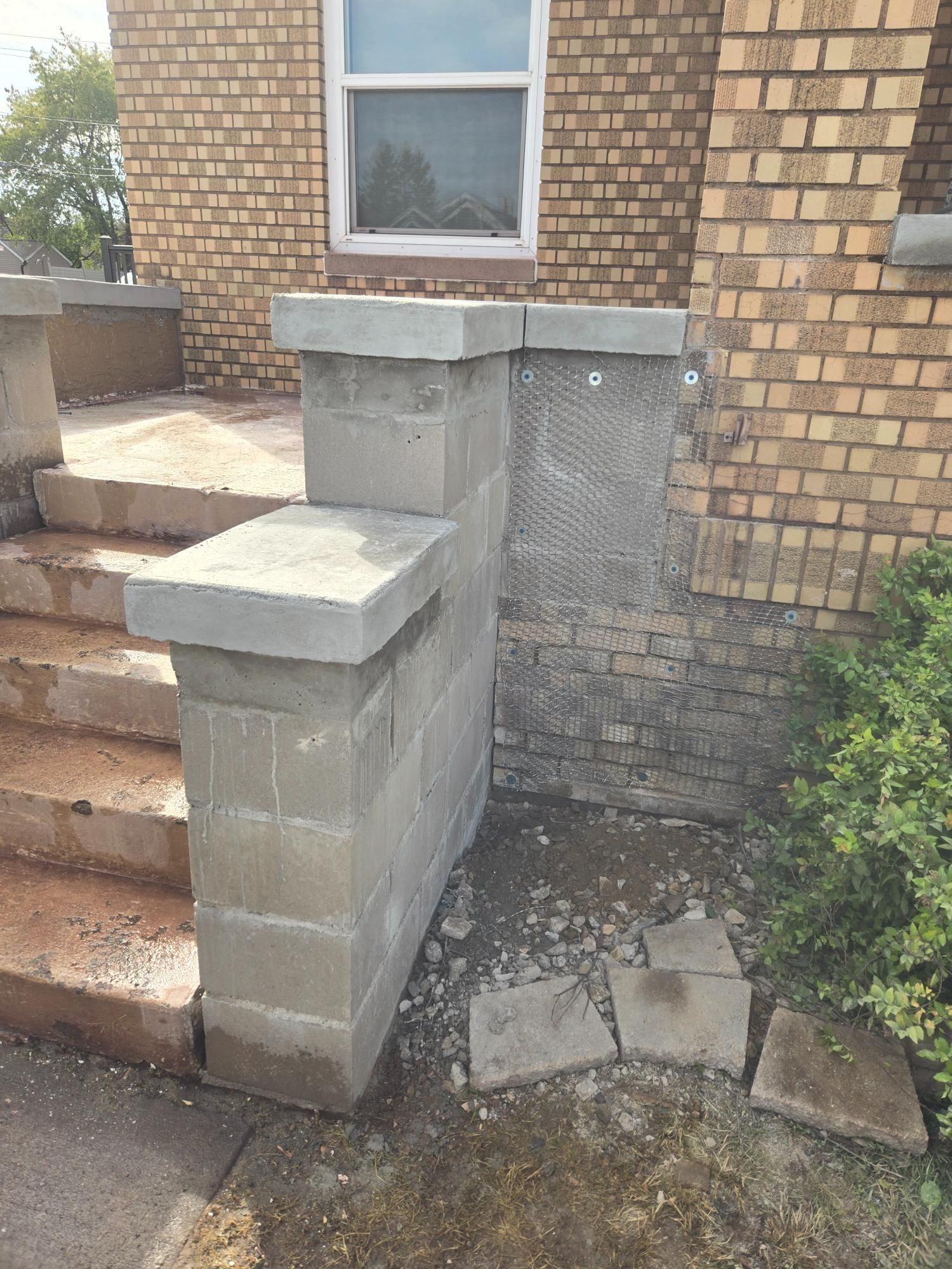 A brick wall with a concrete pillar in front of a brick house.