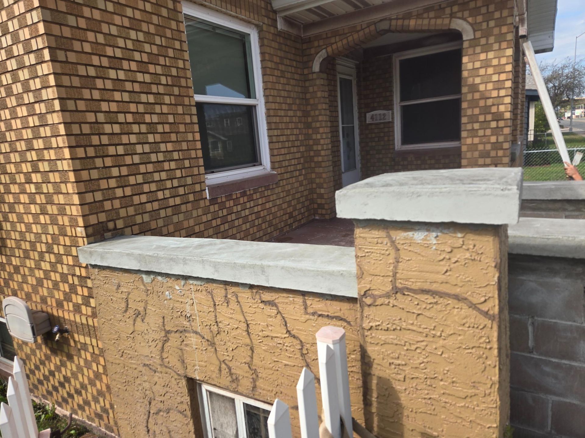A brick house with a porch and a white fence