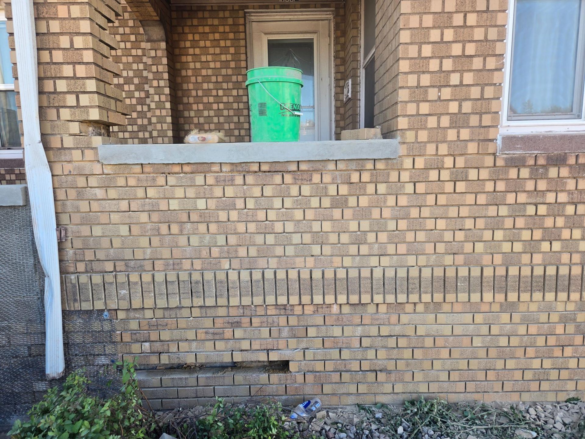 A brick building with a green trash can on the porch.