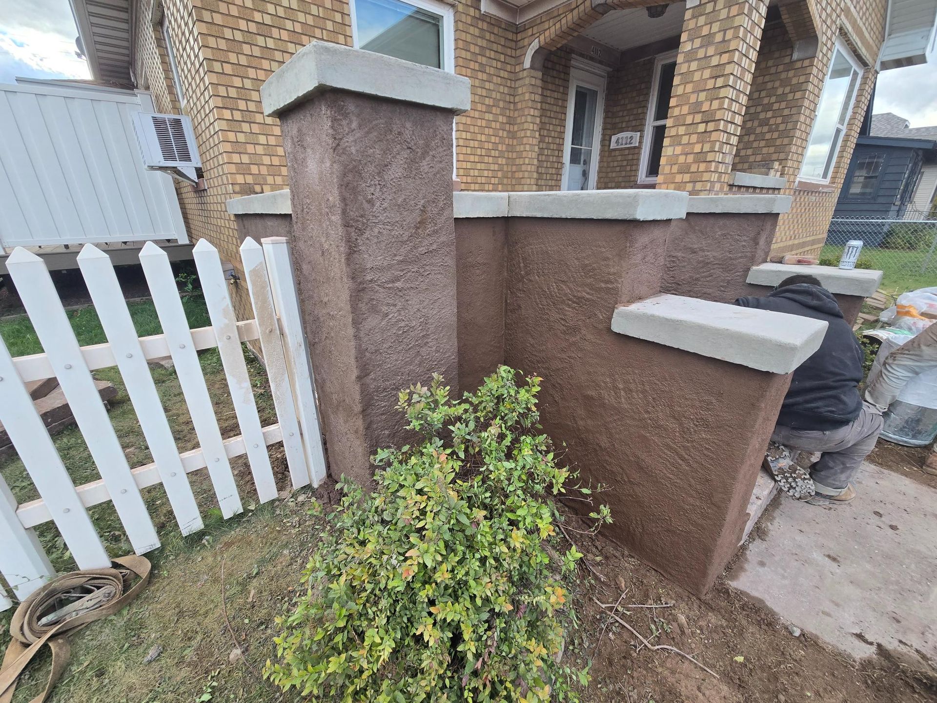 A man is working on a fence in front of a brick house.