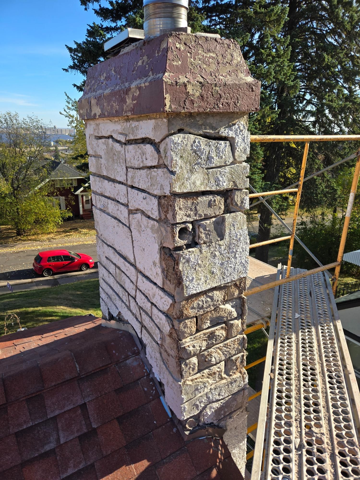 A brick chimney is sitting on top of a roof next to a scaffolding.