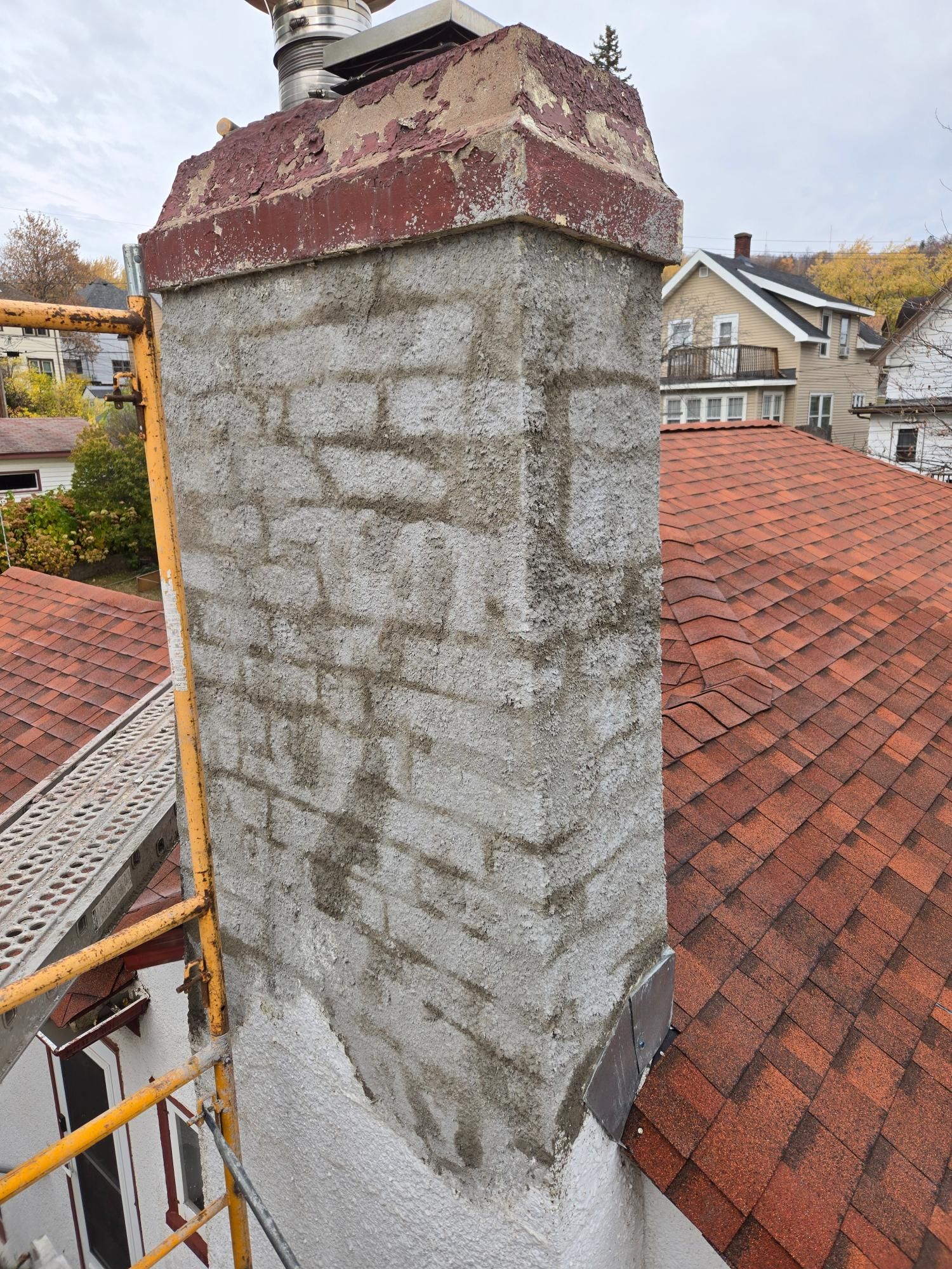 A brick chimney is sitting on top of a roof next to a scaffolding.