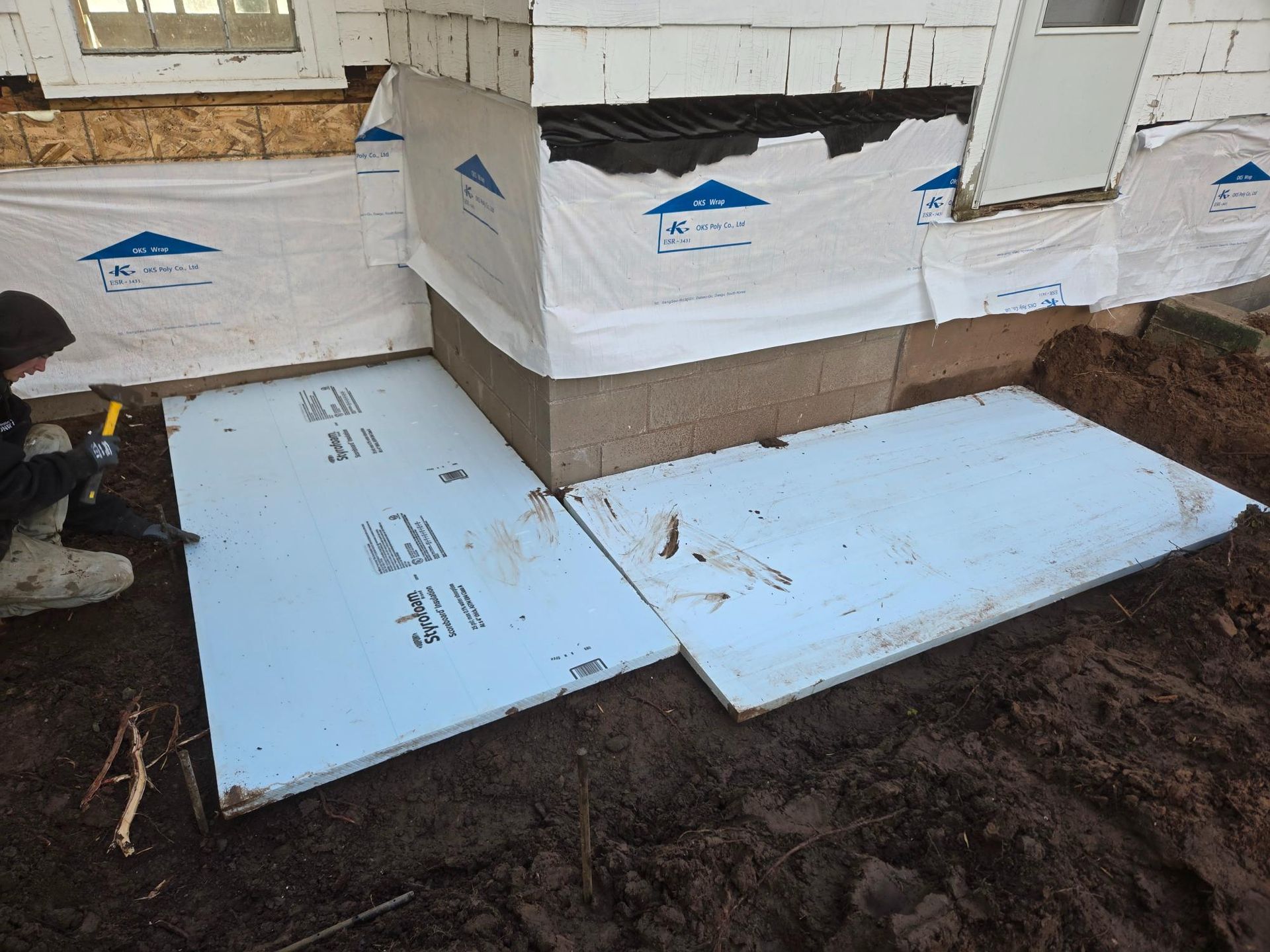 A person is laying styrofoam on the ground in front of a house.