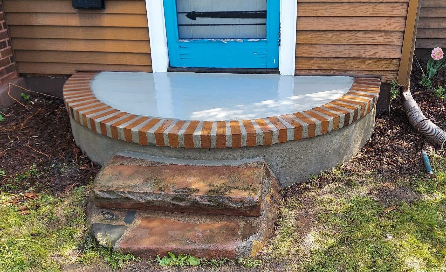 A brick porch with steps and a blue door in front of a house.
