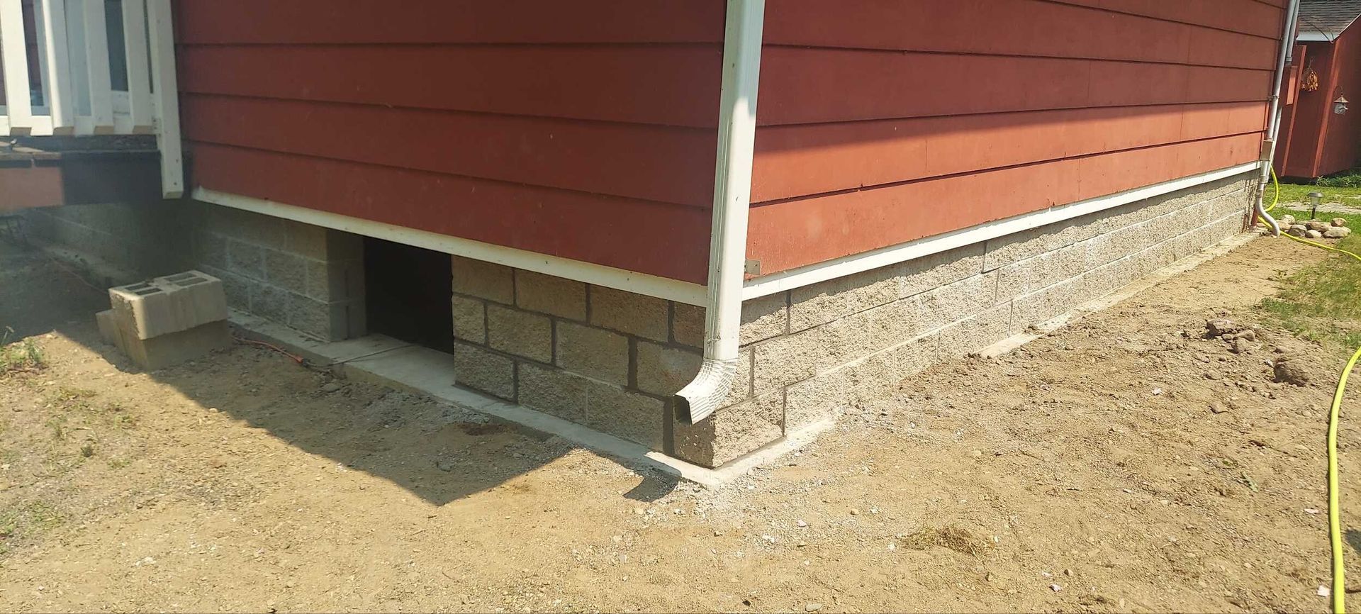 A red house with a brick foundation is sitting on top of a dirt field.