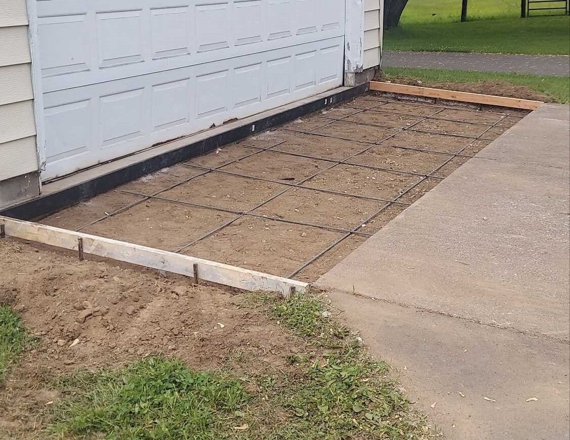 A concrete walkway is being built next to a garage door.