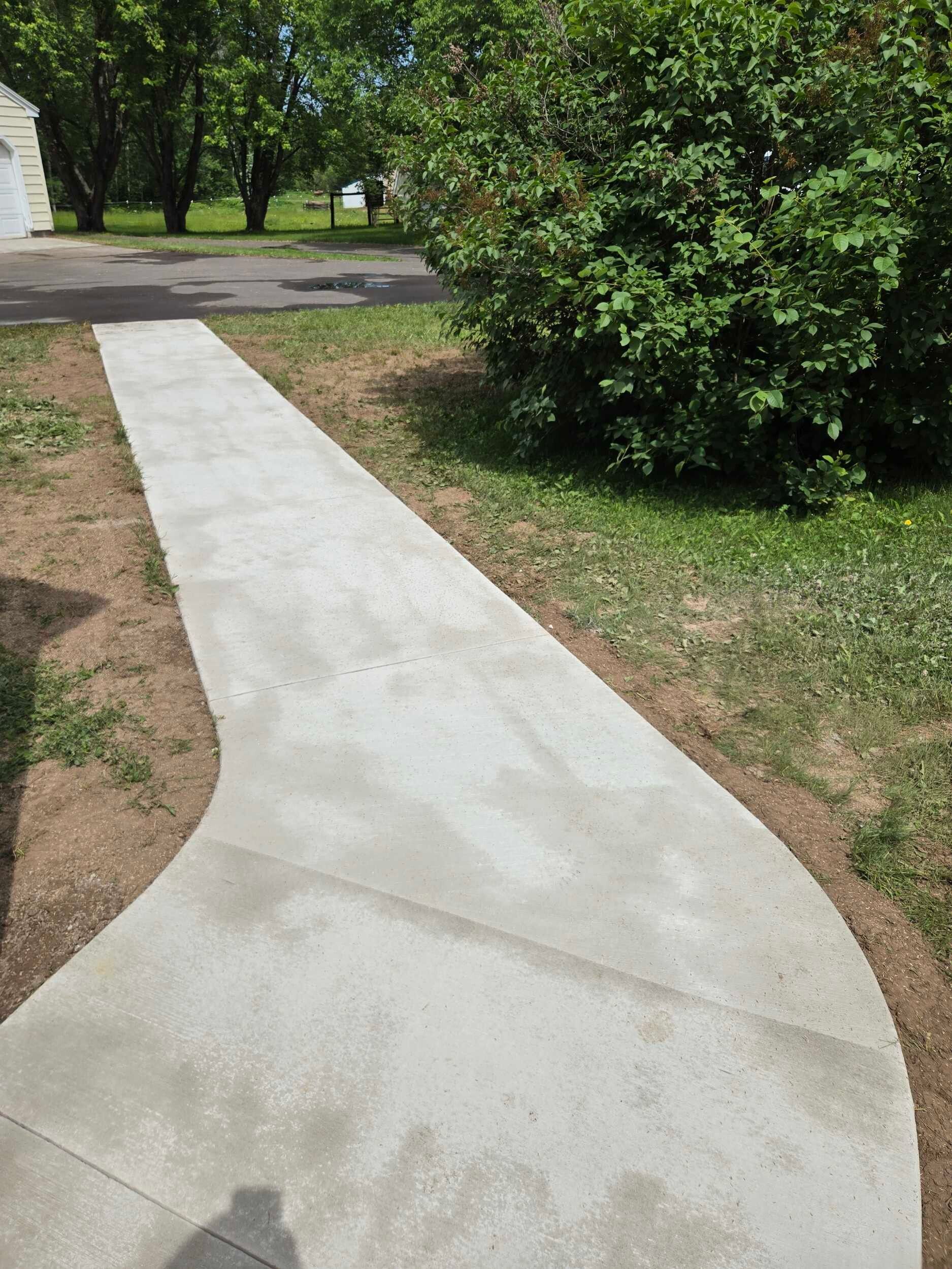 A concrete walkway leading to a house with trees in the background.