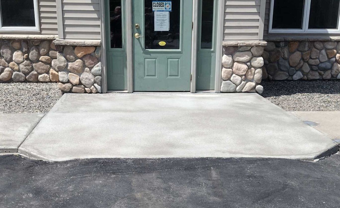 A stone building with a green door and a concrete walkway