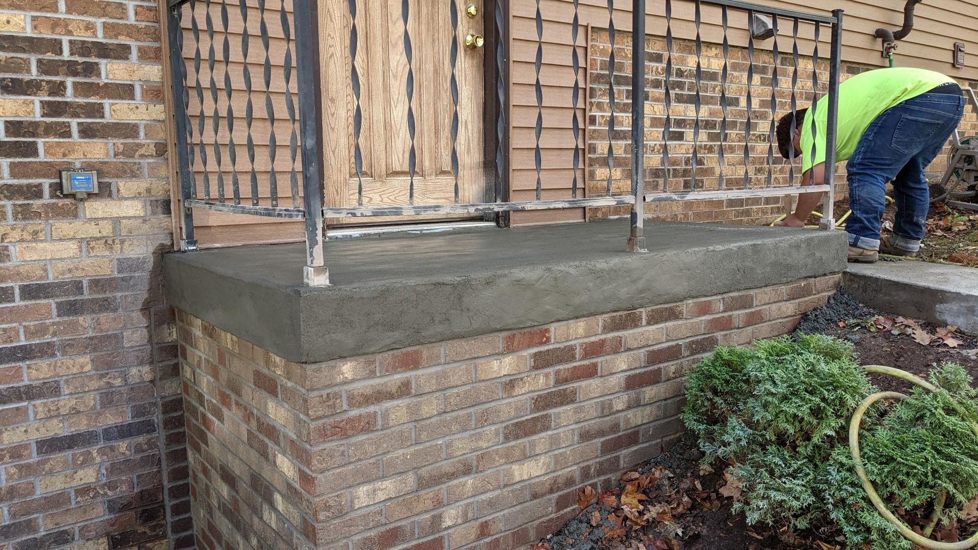 A man is working on a concrete porch in front of a brick building.