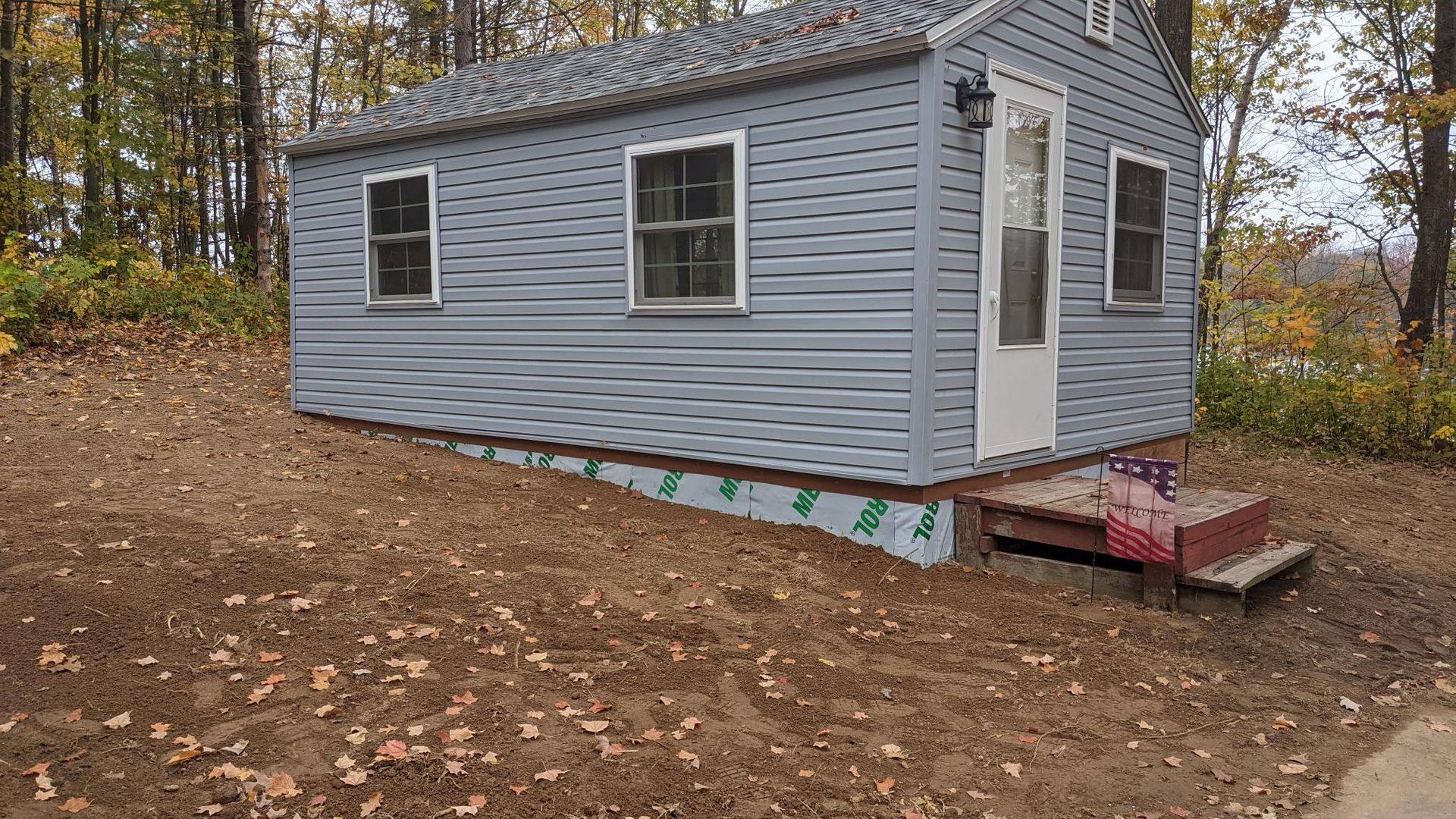 A small house is sitting on top of a dirt hill in the middle of a forest.