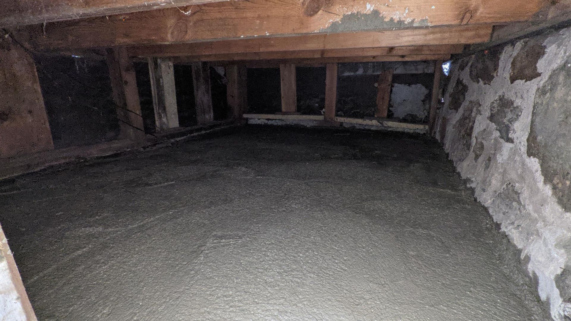 A basement with a lot of concrete and wooden beams.