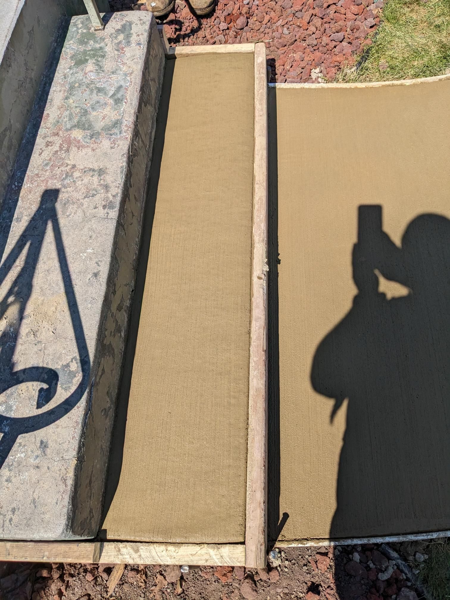 A person is taking a picture of their shadow on a concrete surface.