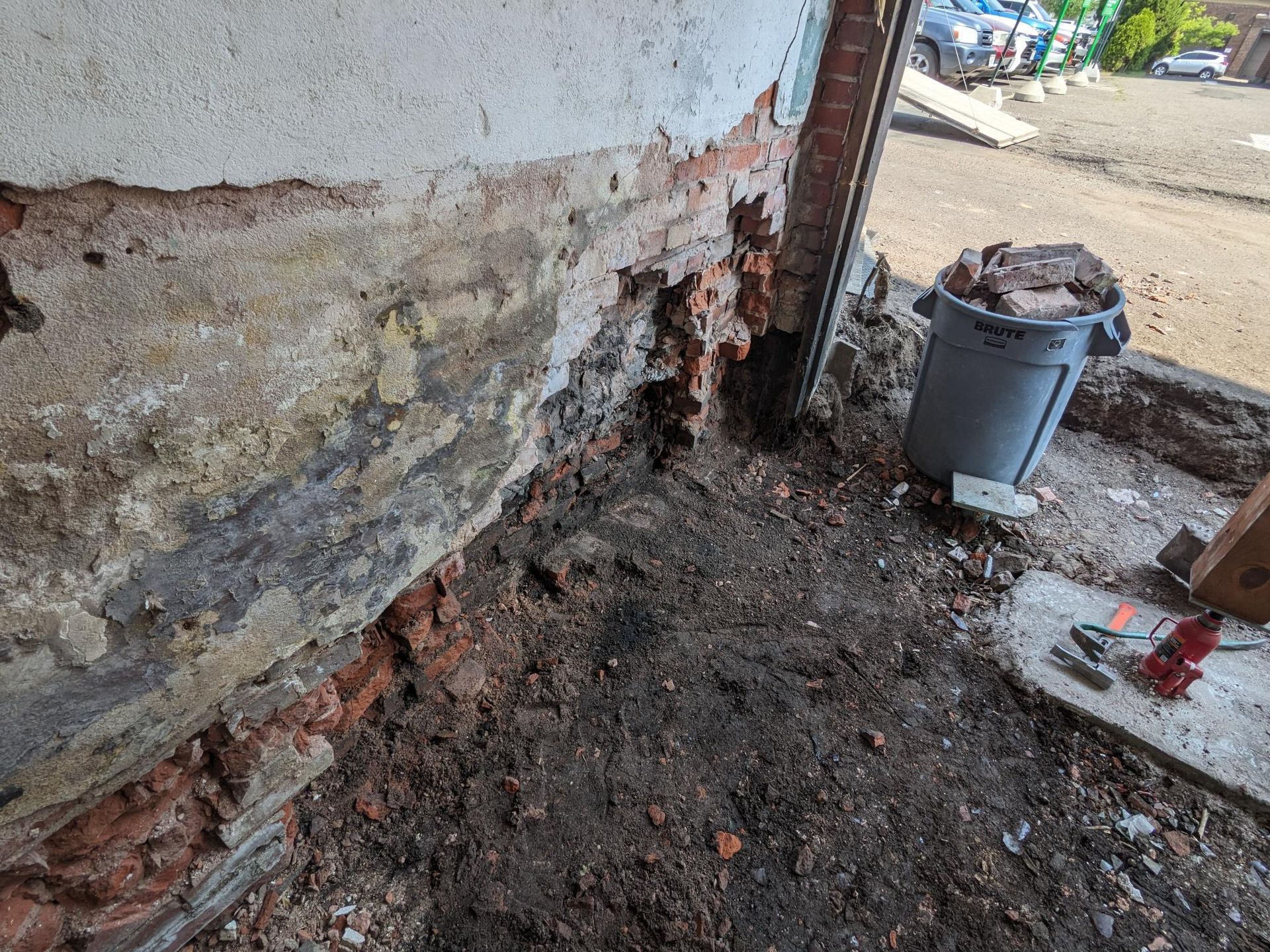 A bucket of dirt is sitting next to a brick wall.