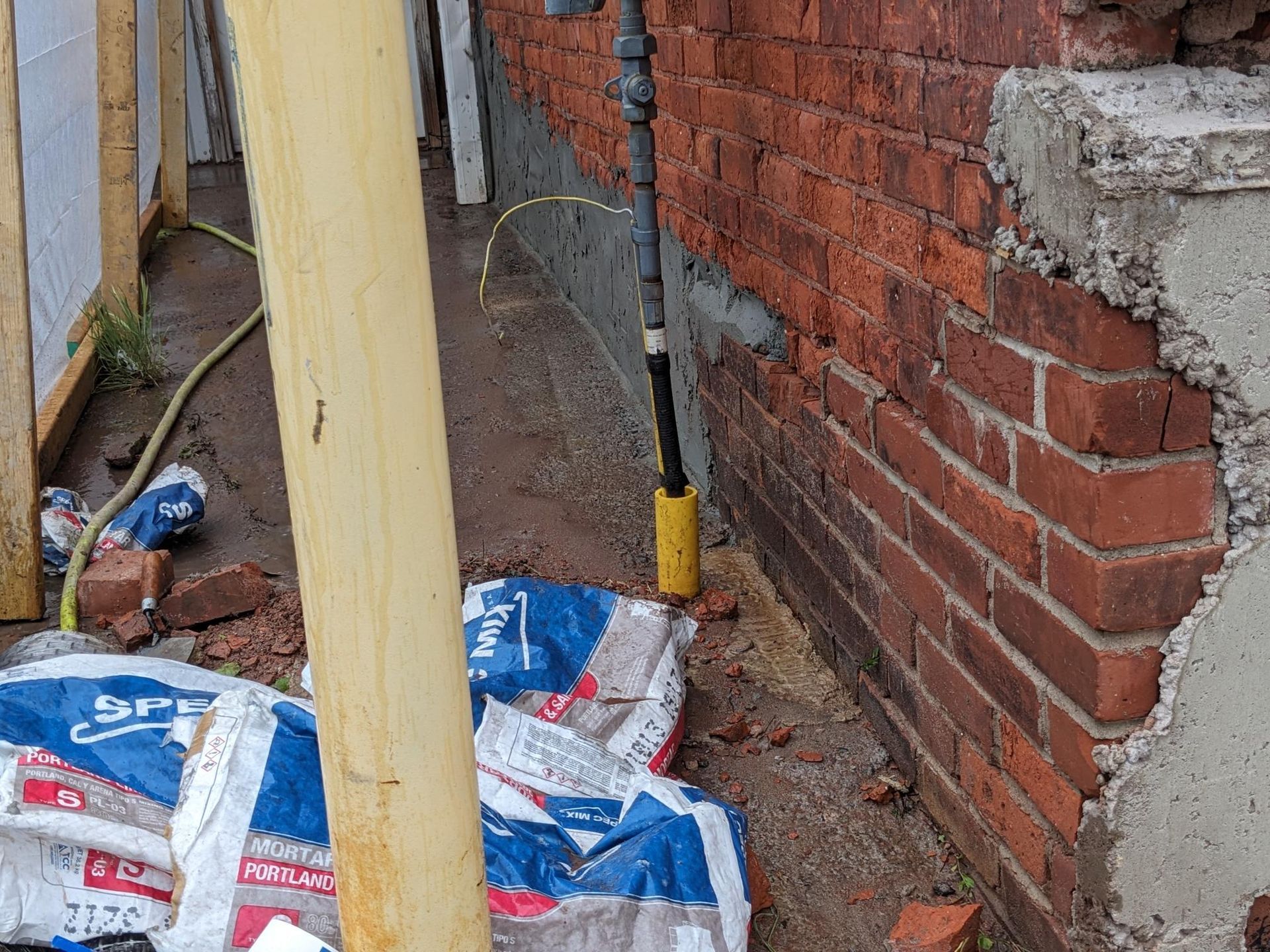 A bag of cement is laying on the ground next to a brick wall