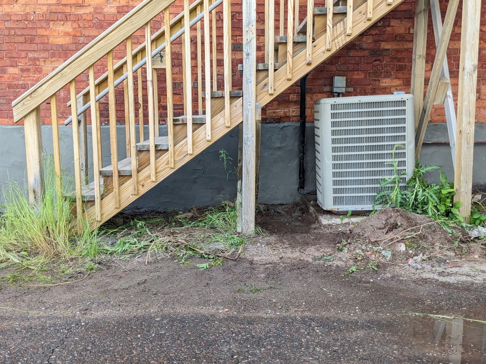 A wooden staircase next to a brick building with an air conditioner.
