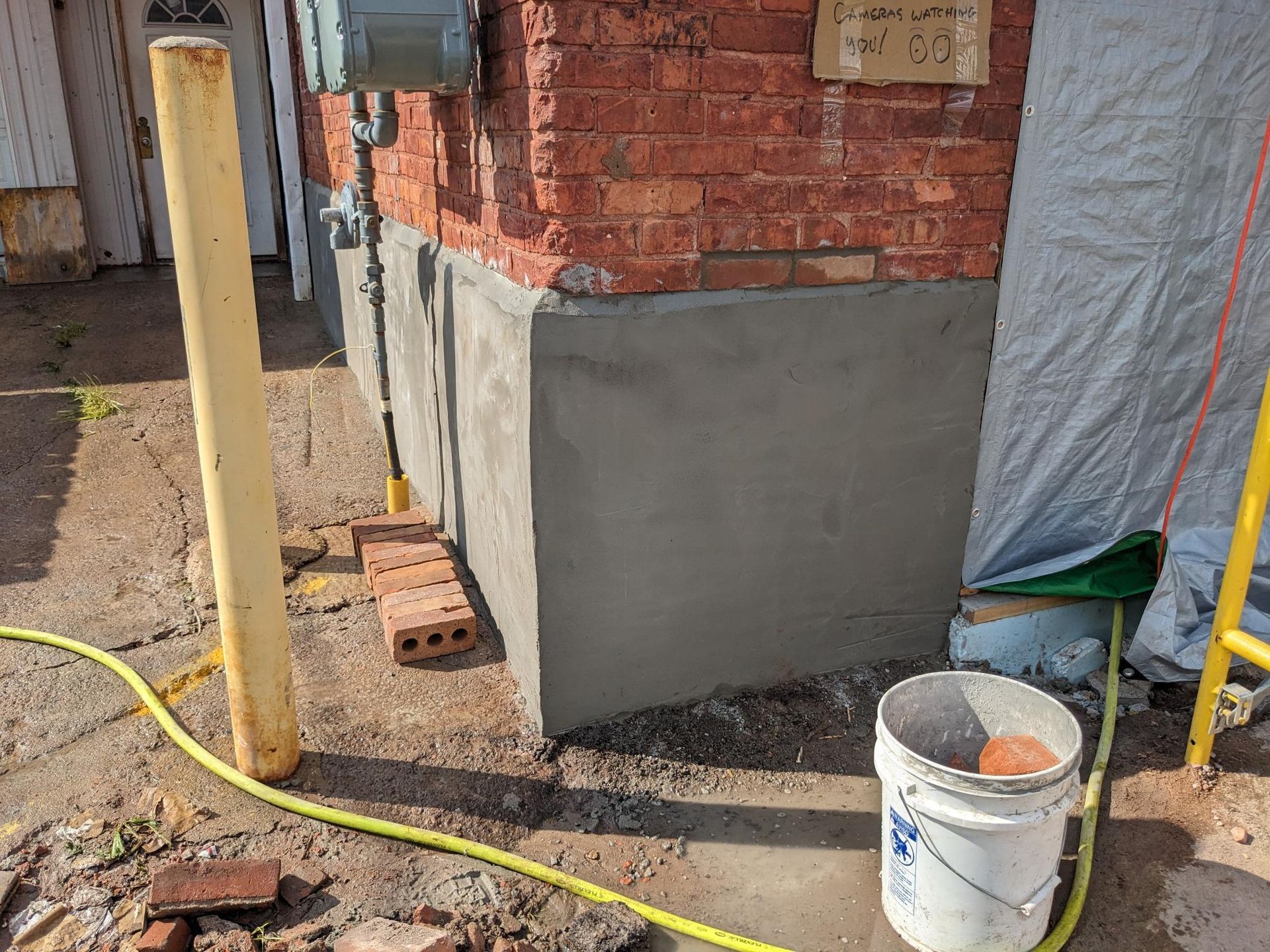 A bucket of concrete is sitting on the ground in front of a brick building.