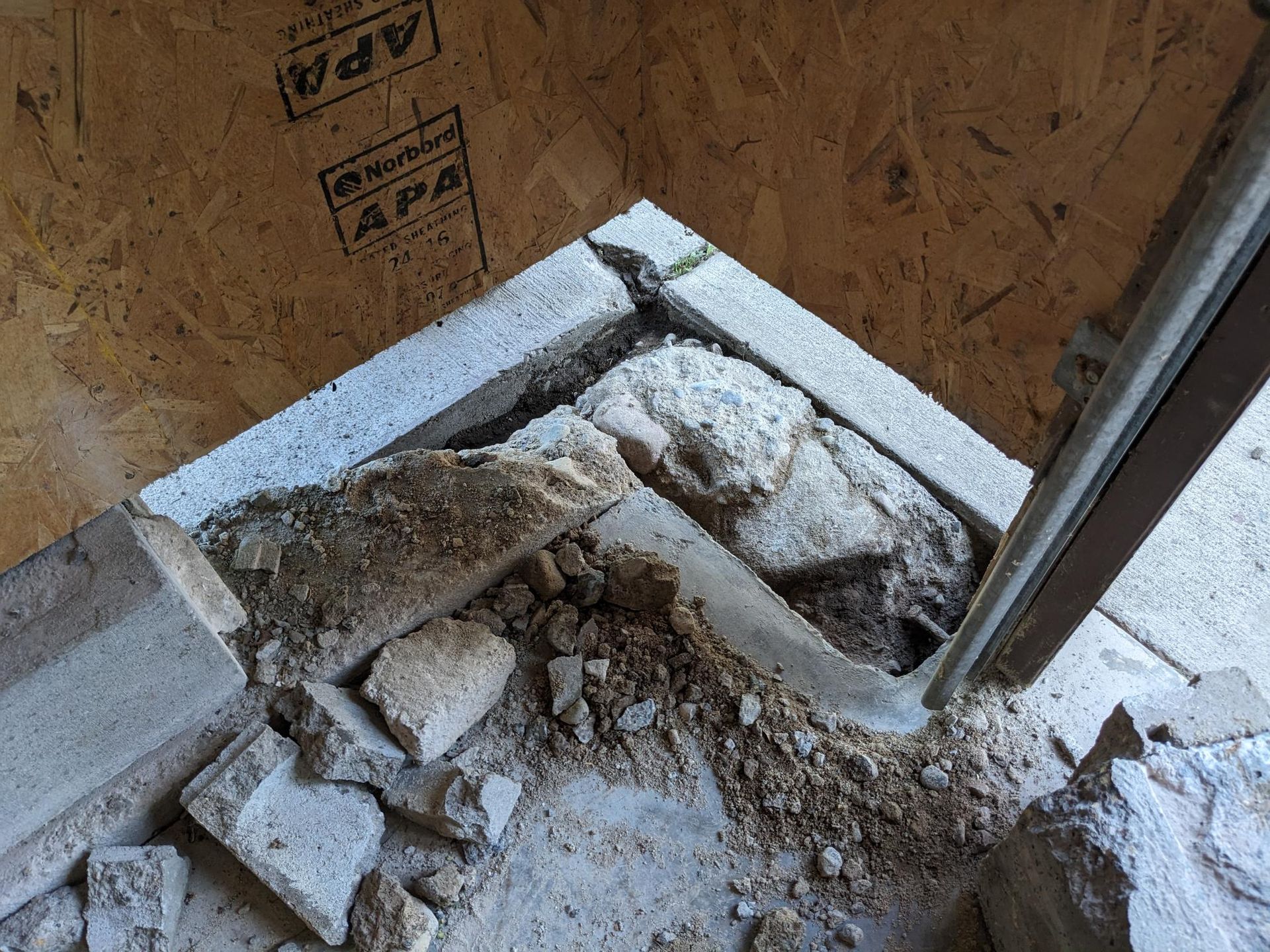 A pile of rocks is laying on the ground in front of a wooden wall.
